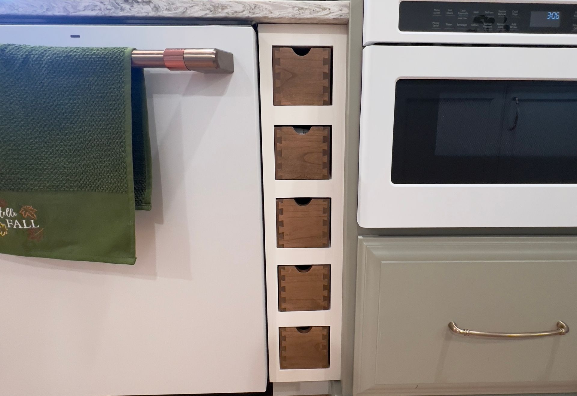 A kitchen view showing a narrow, vertical rack with five stacked wooden drawers between a dishwasher and a wall oven.