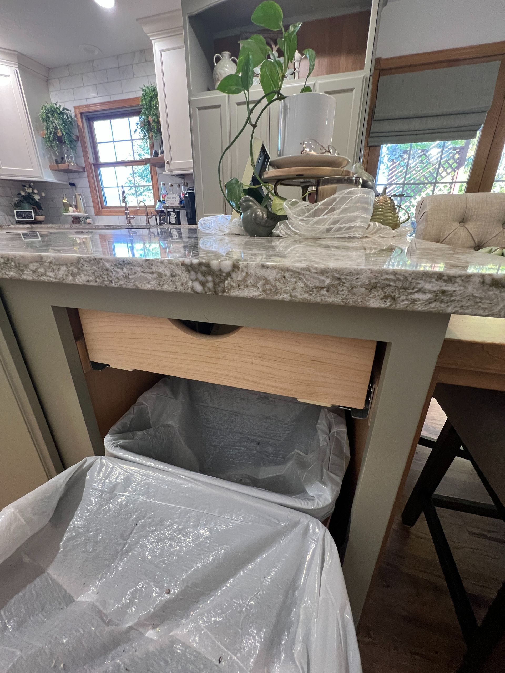 A kitchen island with a slide-out drawer open, revealing two plastic bins lined with white trash bags.