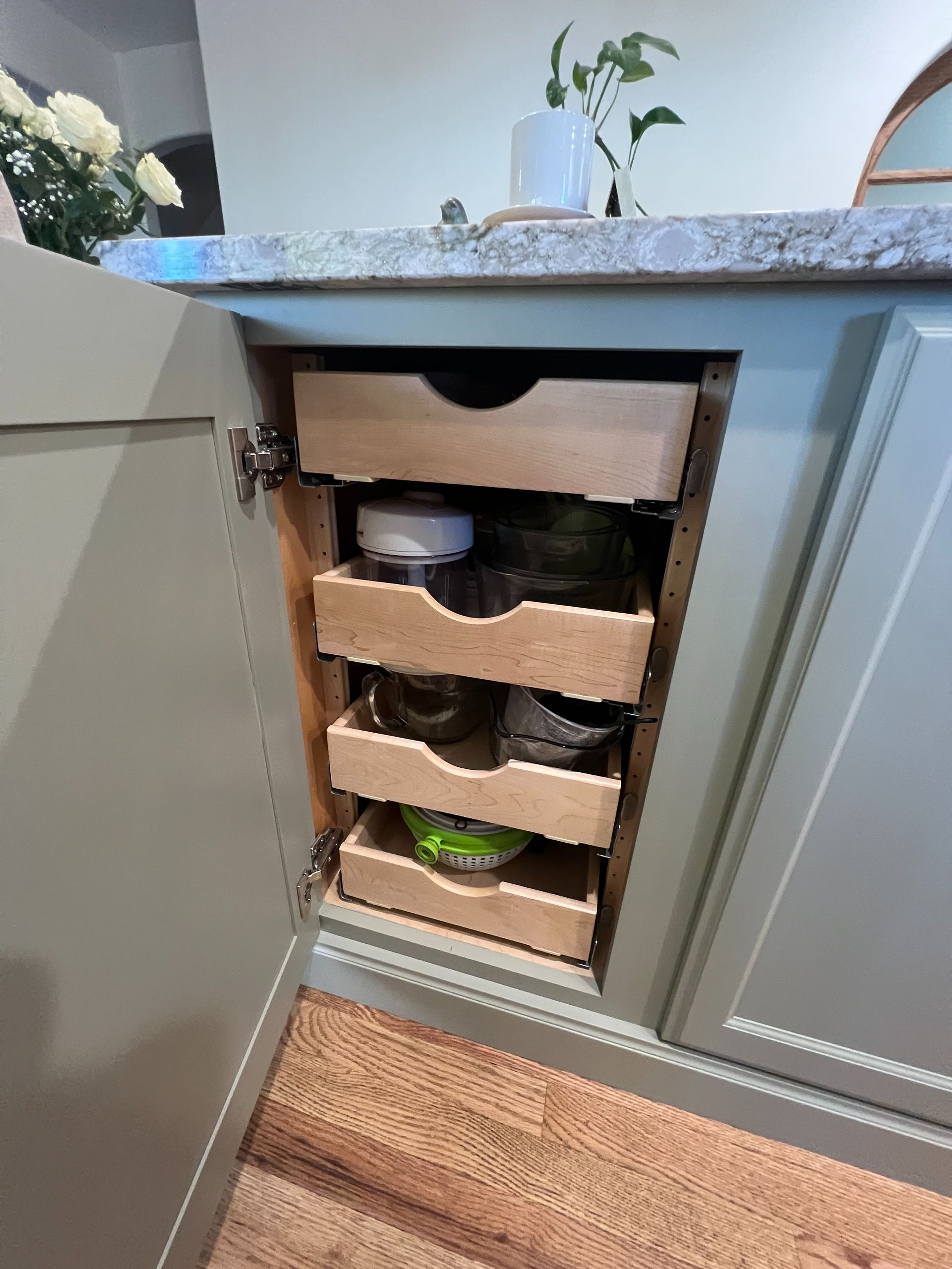 A pull-out pantry cabinet with four wooden sliding drawers inside a light green kitchen base cabinet.