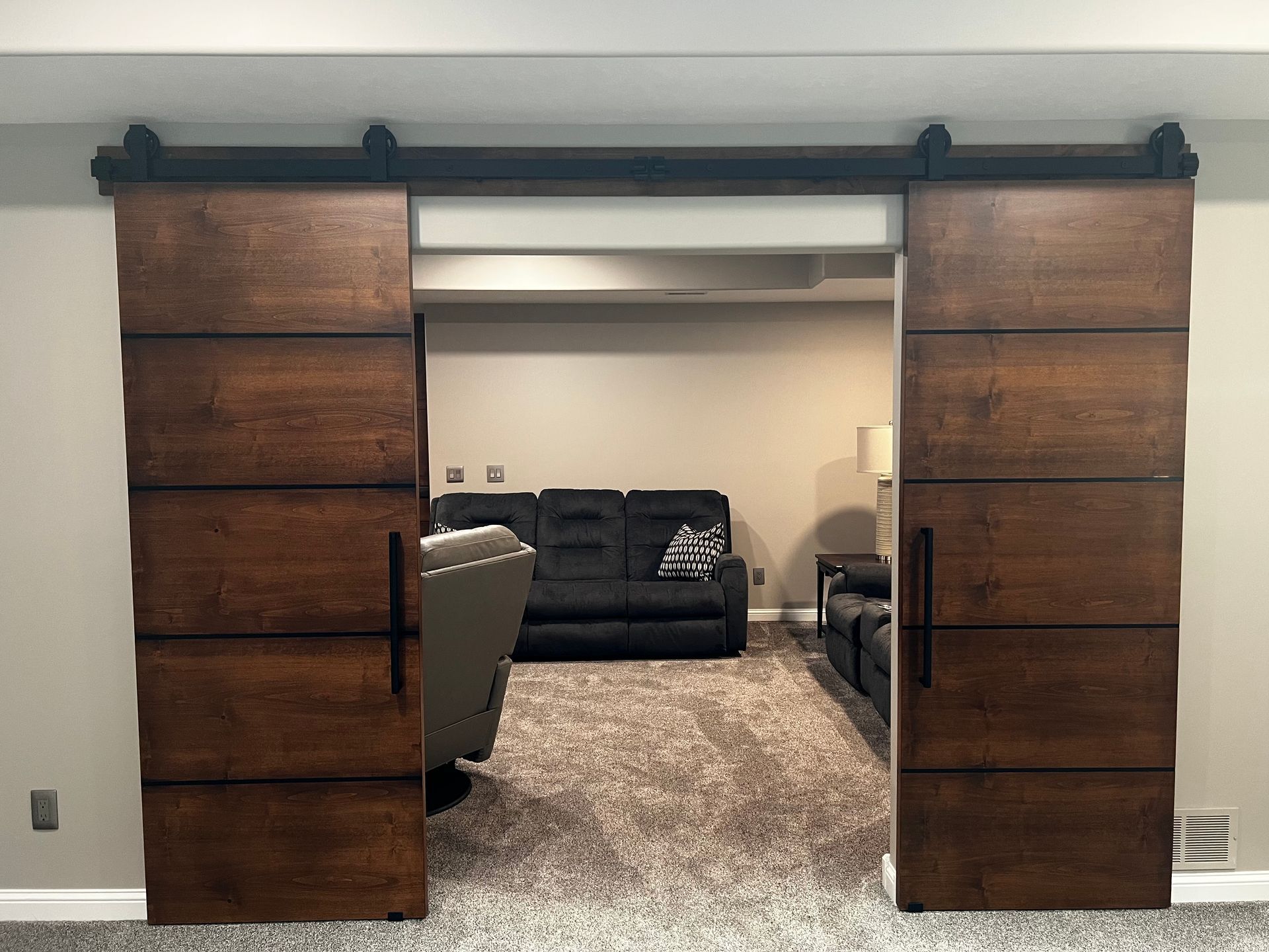Two dark wood sliding barn doors installed in a light-colored room, opening to a view of a living area with a sofa.