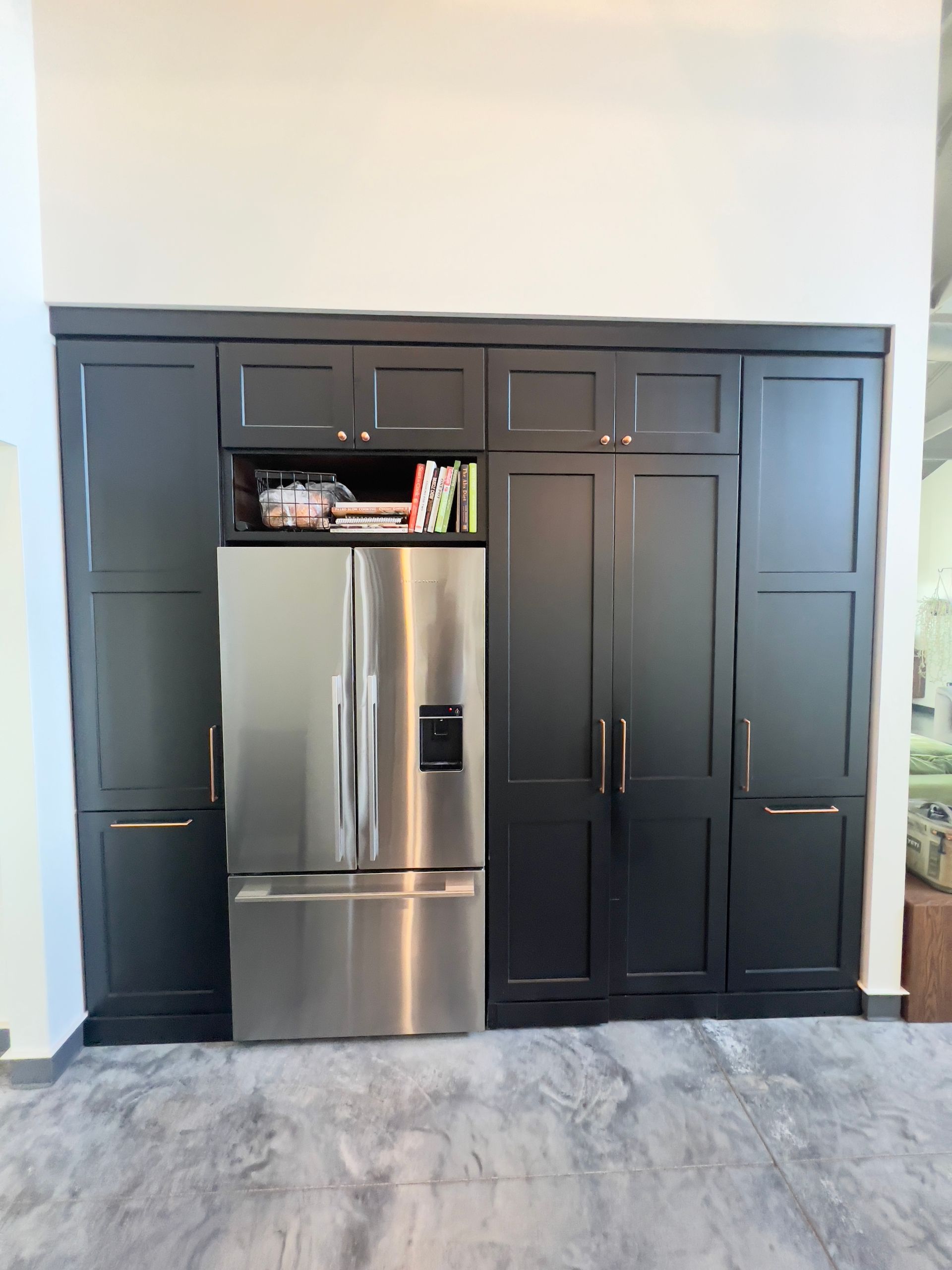 A stainless steel refrigerator built into a wall of dark, matte black cabinetry with integrated storage.