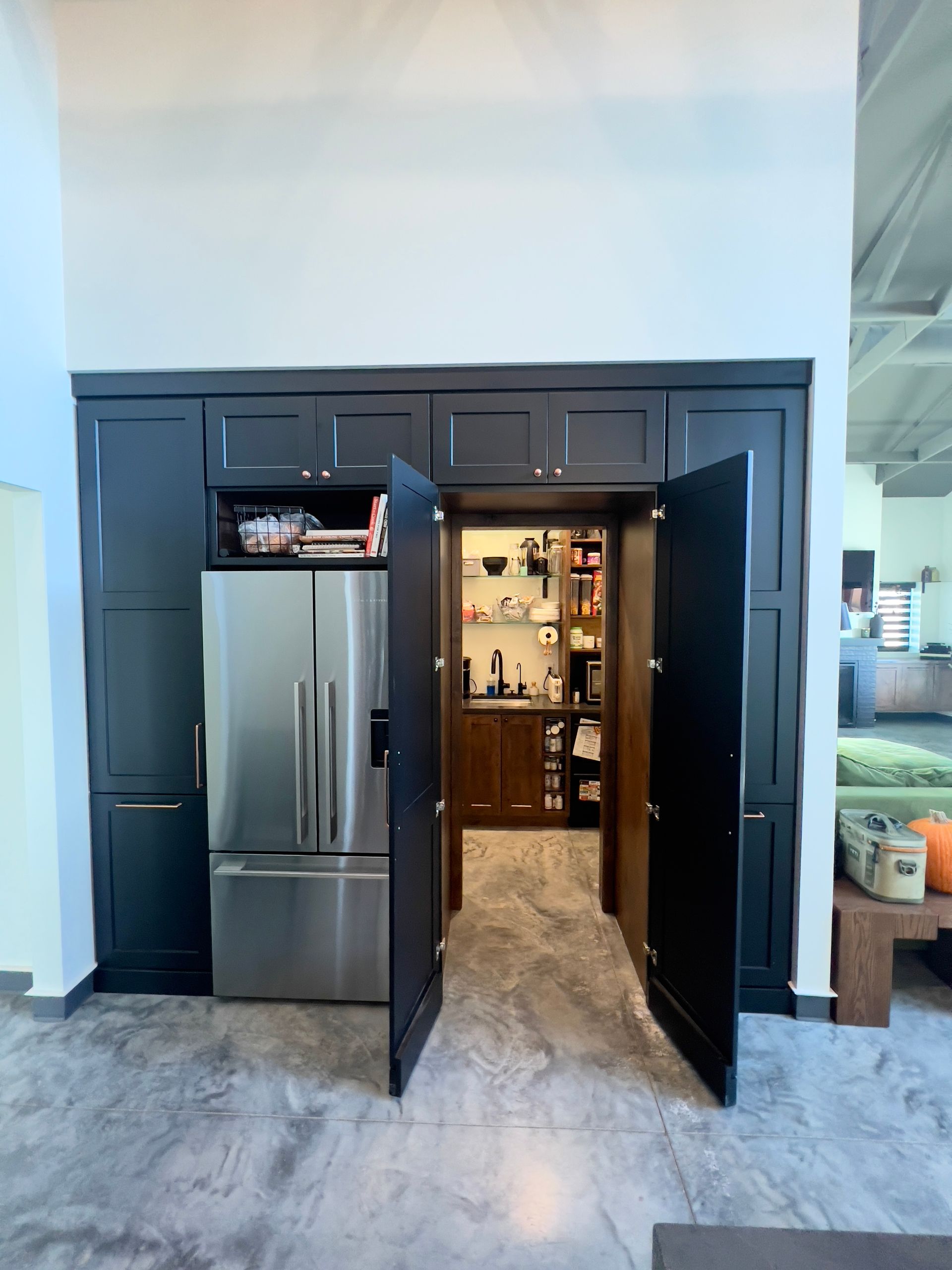 A black cabinet wall with an integrated stainless steel refrigerator and an open doorway leading to a walk-in pantry.