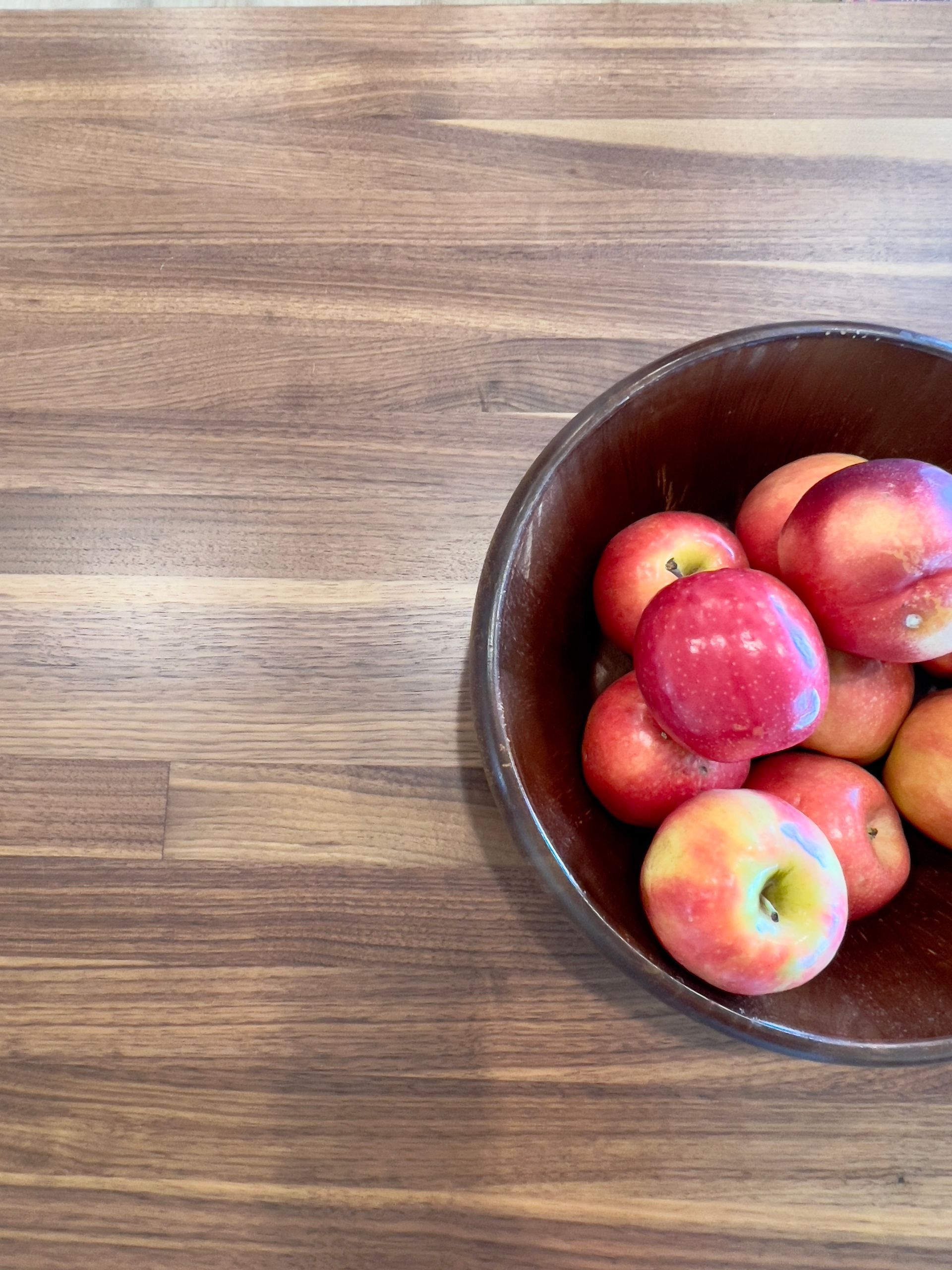 A wooden bowl filled with fresh red apples sits on a wooden kitchen counter.