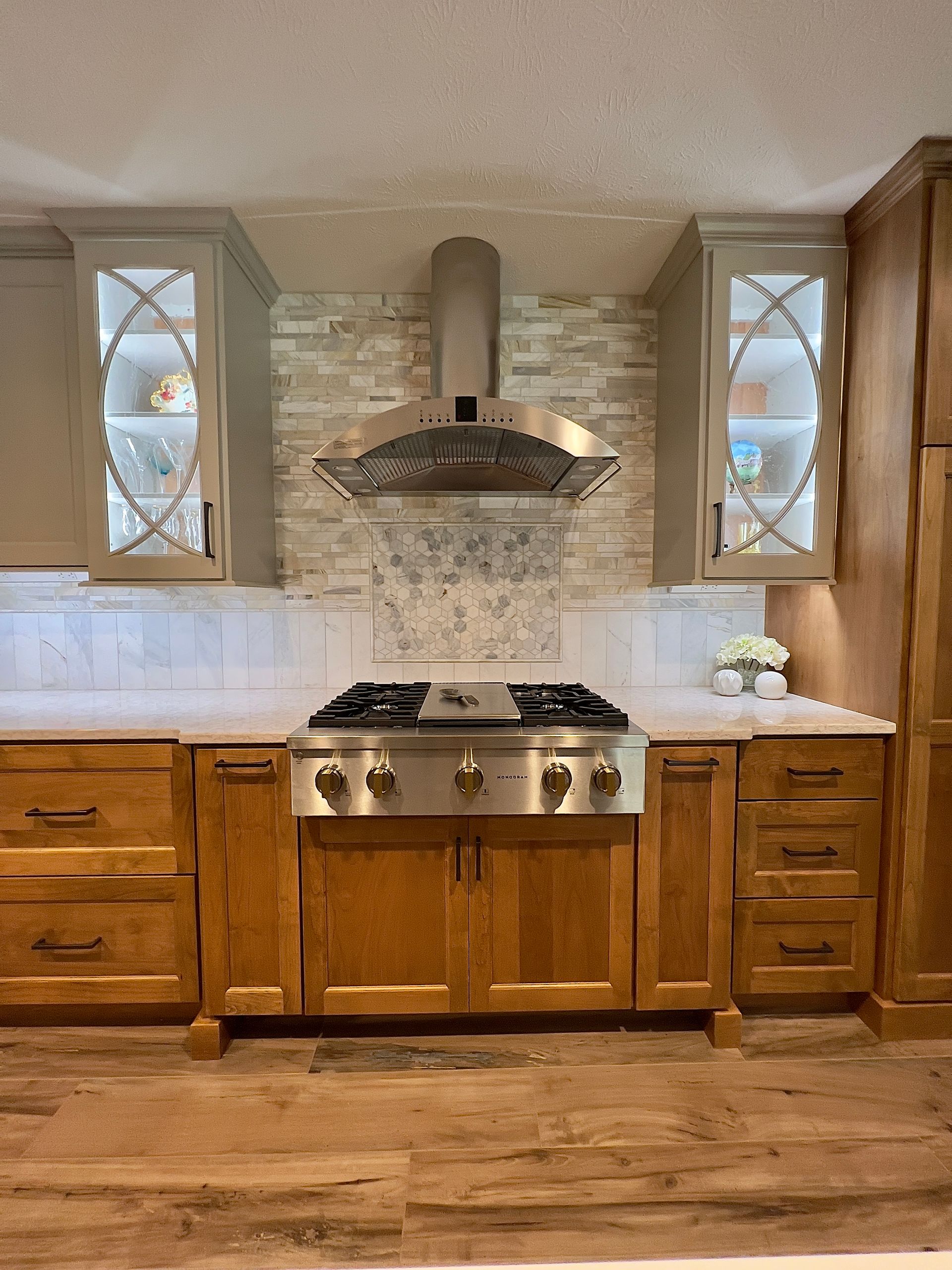 A kitchen stove area with wood cabinets, a stainless steel range and hood, and decorative glass-front upper cabinets.