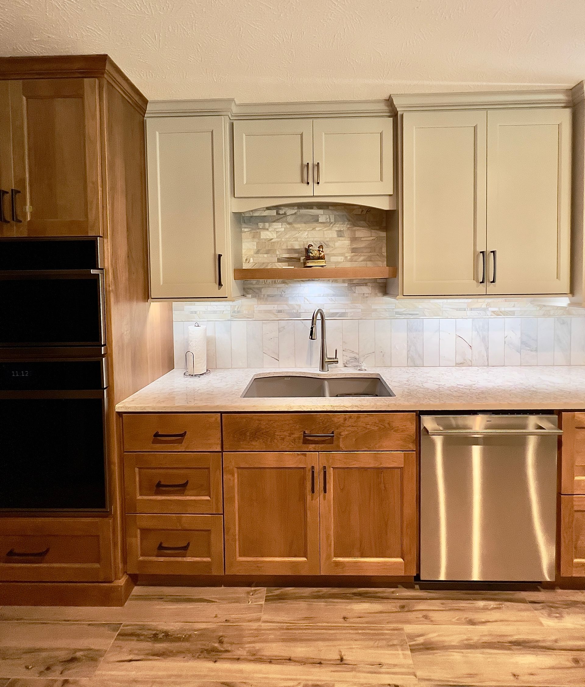 A kitchen counter with a stainless steel dishwasher and sink, featuring light-colored upper cabinets and wood base cabinets.