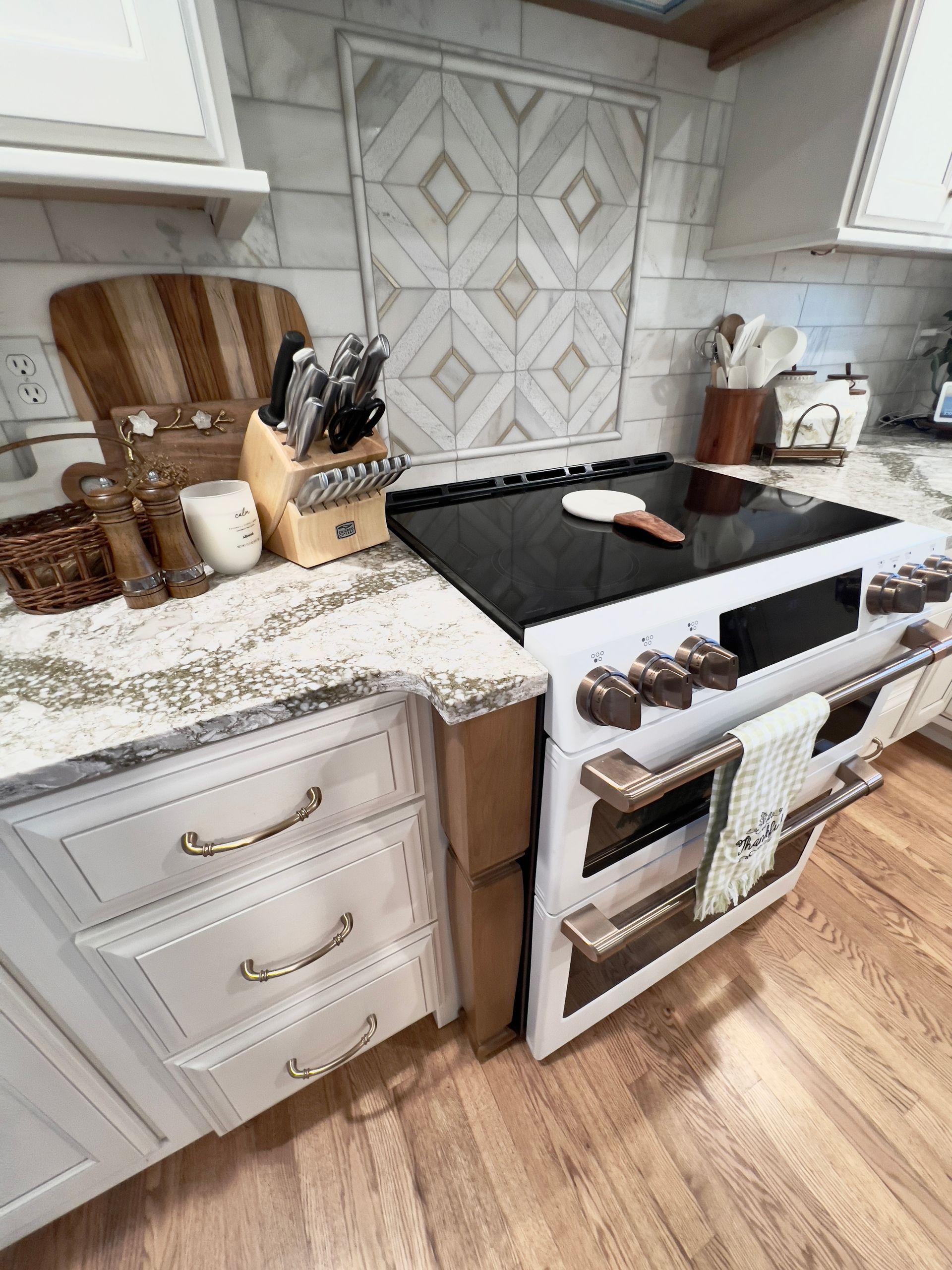 A kitchen with white cabinets, granite countertops, a white oven, and a decorative tile backsplash behind the stove.
