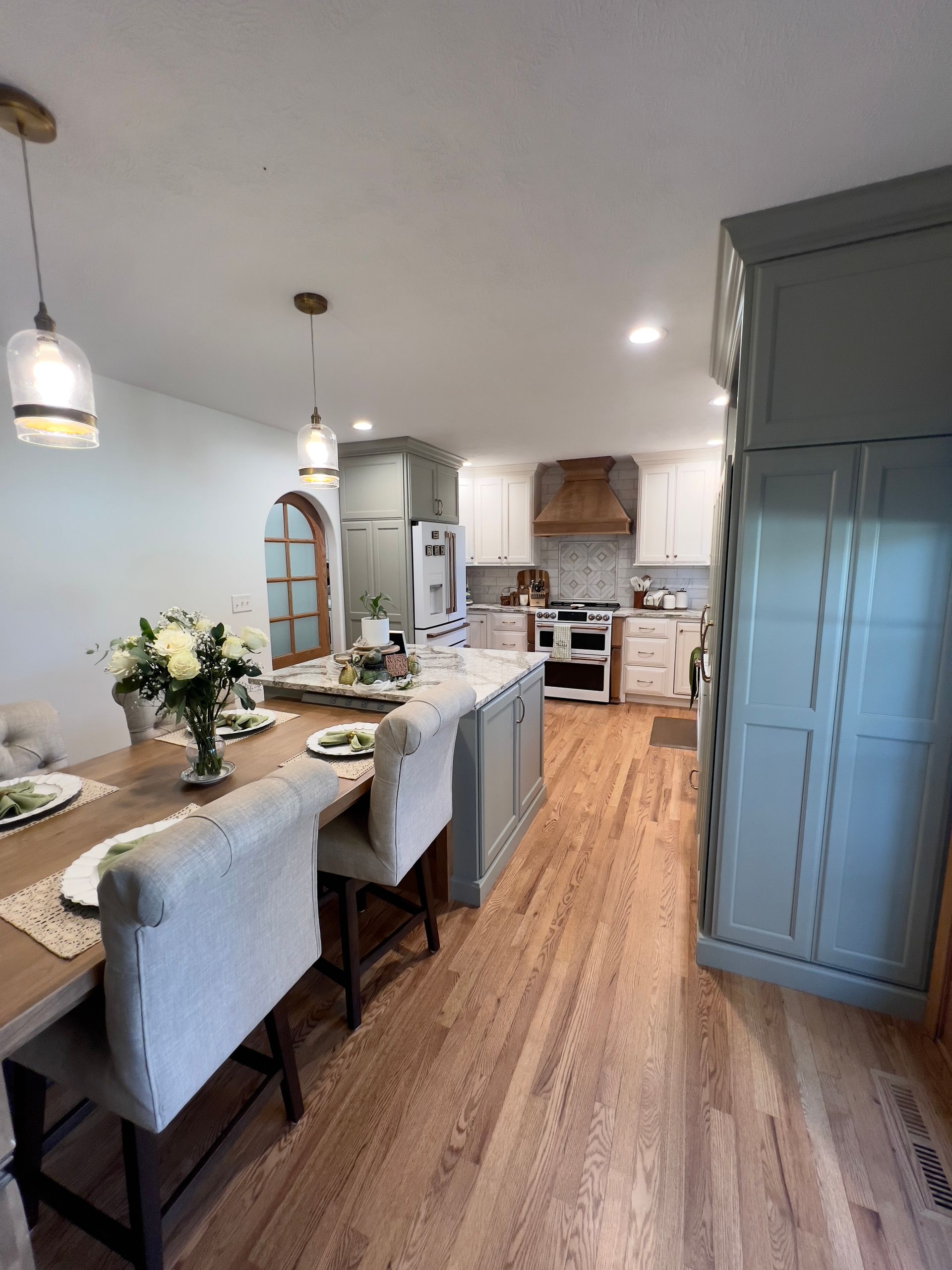 A dining table with cream chairs sits in an open-concept kitchen with light blue cabinetry and light wood floors.