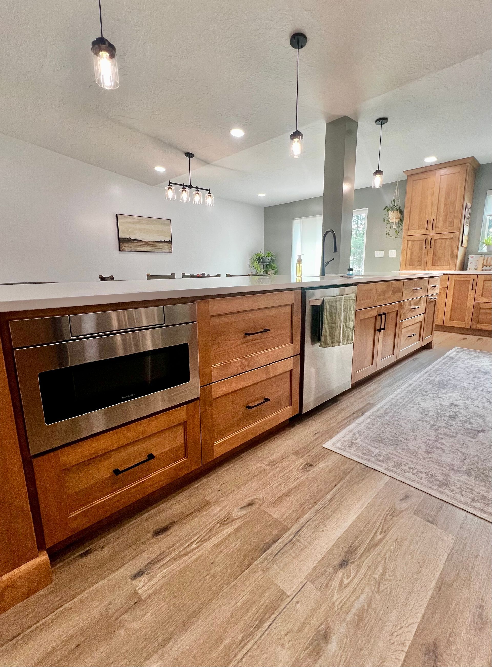 A kitchen island with wood cabinets, a built-in microwave, and stainless-steel appliances on light hardwood floors.