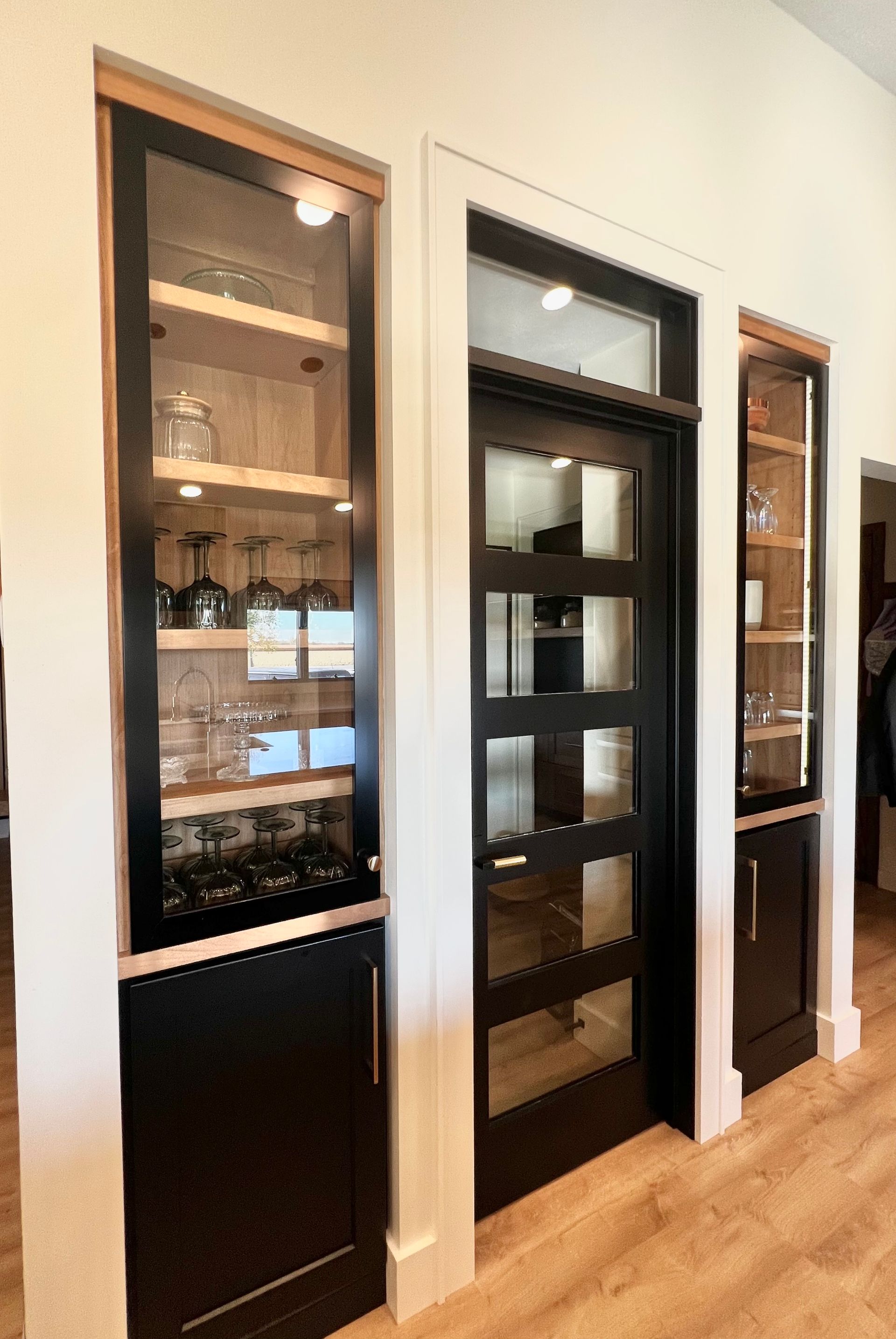 A black door with glass panels sits between two built-in black cabinets with glass-front display shelves.