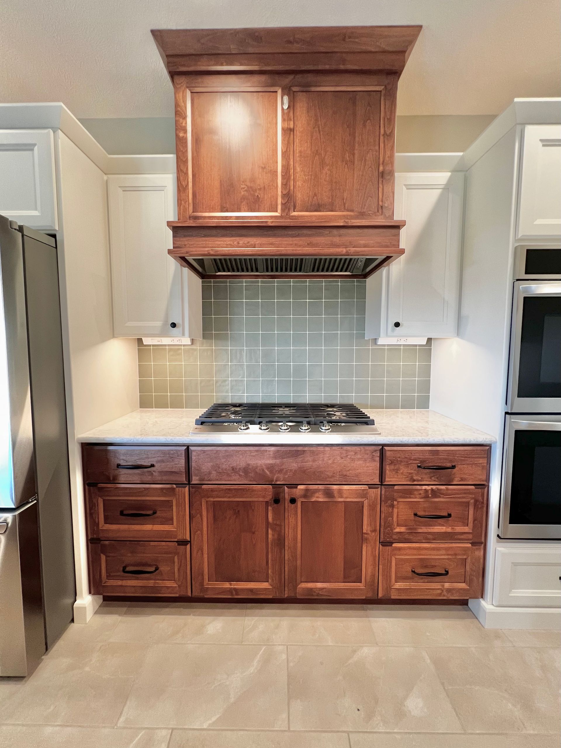 Kitchen stove area with white cabinets, a central wooden vent hood, a matching wooden base cabinet, and gray tile backsplash.