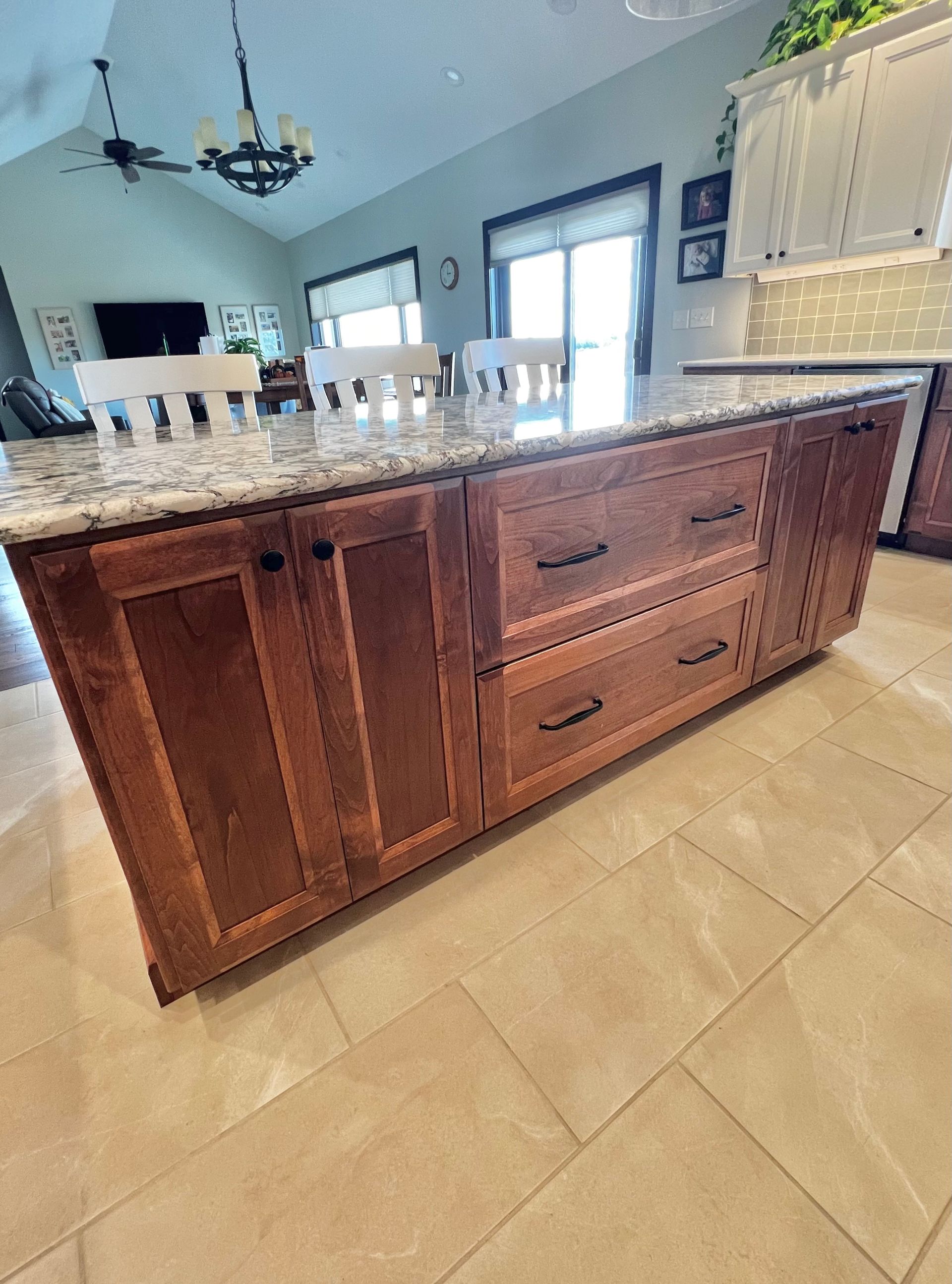 A granite-topped kitchen island with wood cabinets and drawers in a bright, open-concept home.