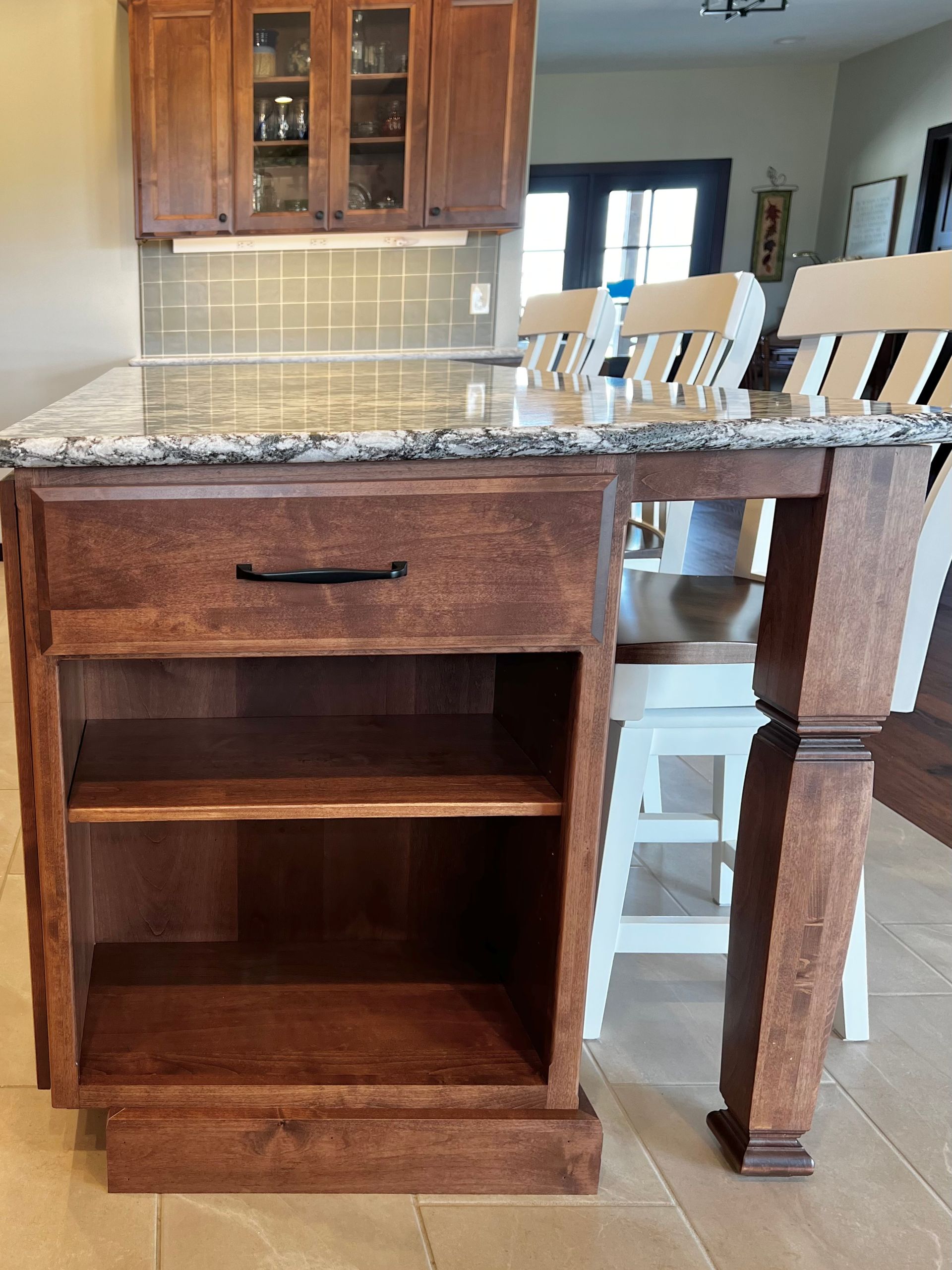 A kitchen island featuring dark wood cabinetry with an open shelf, a granite countertop, and matching wooden stools.