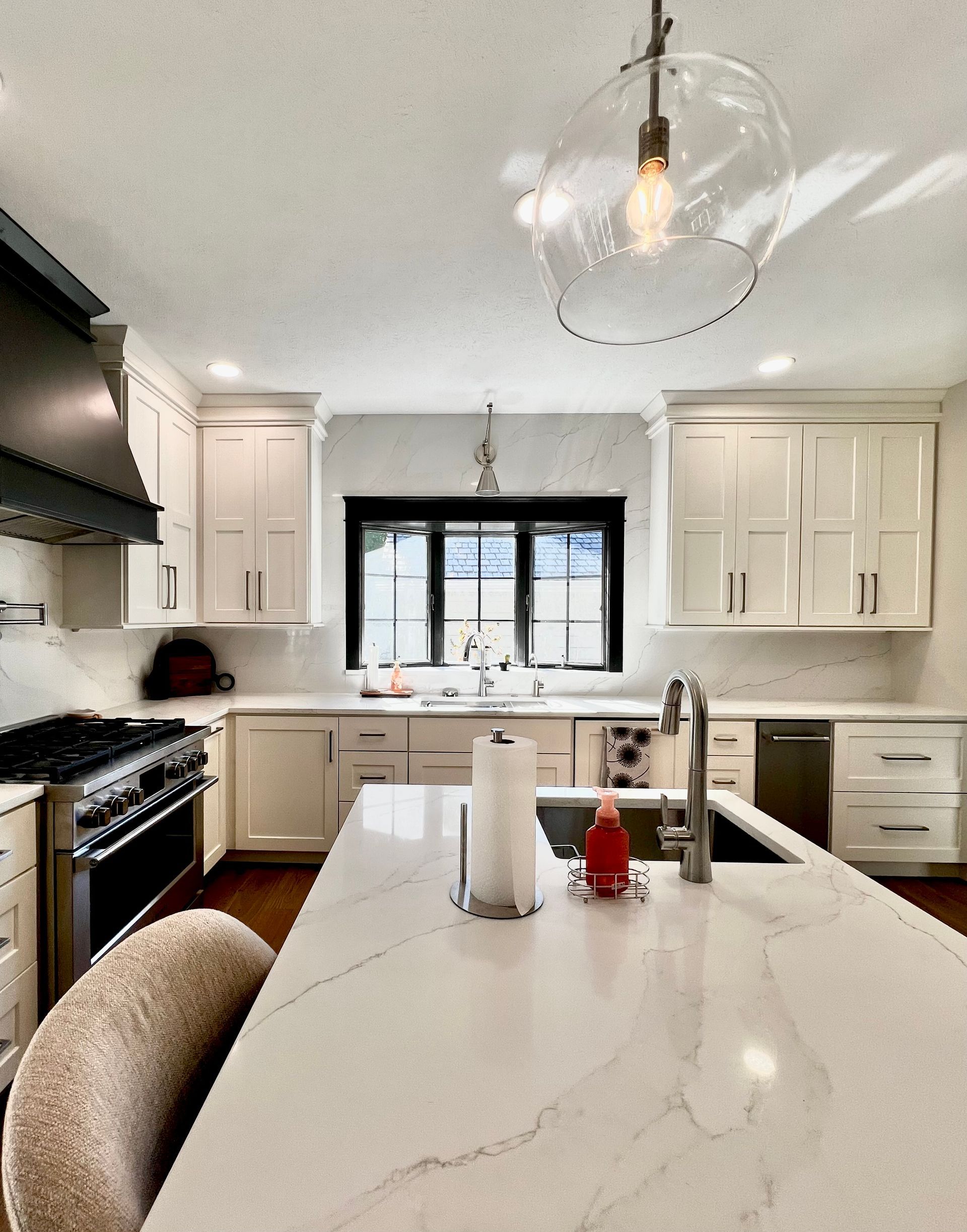 A bright, modern kitchen with white cabinets, a large island with white marble countertops, and a black range hood.