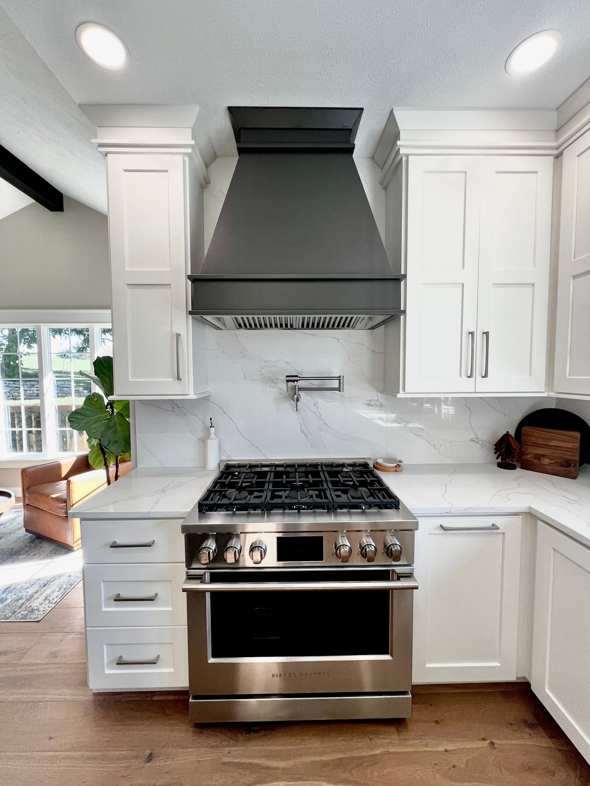 A stainless steel gas stove beneath a black range hood in a kitchen with white cabinetry and a marble backsplash.
