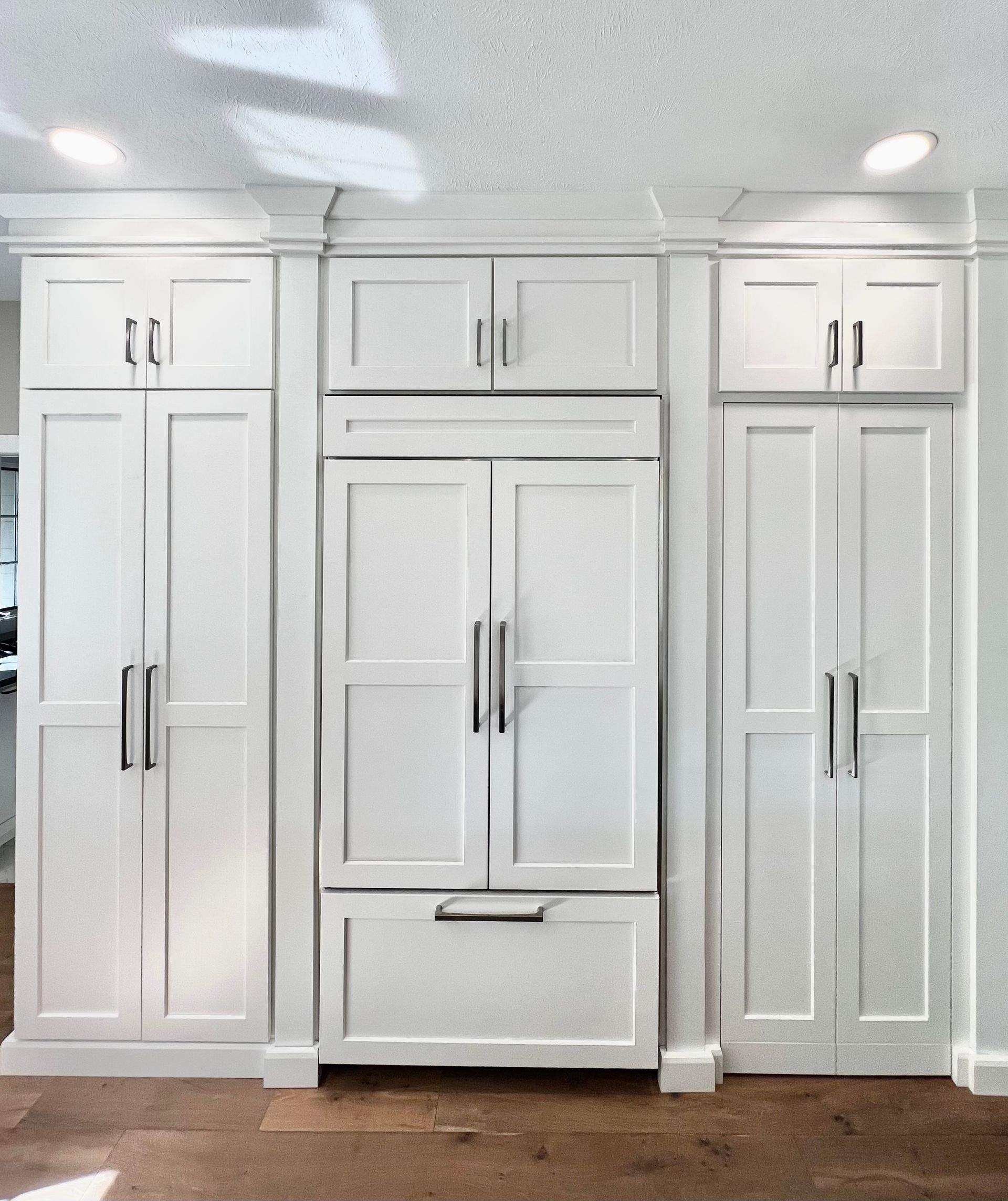 Three sections of white kitchen cabinetry, including a central built-in refrigerator with matching custom panels.