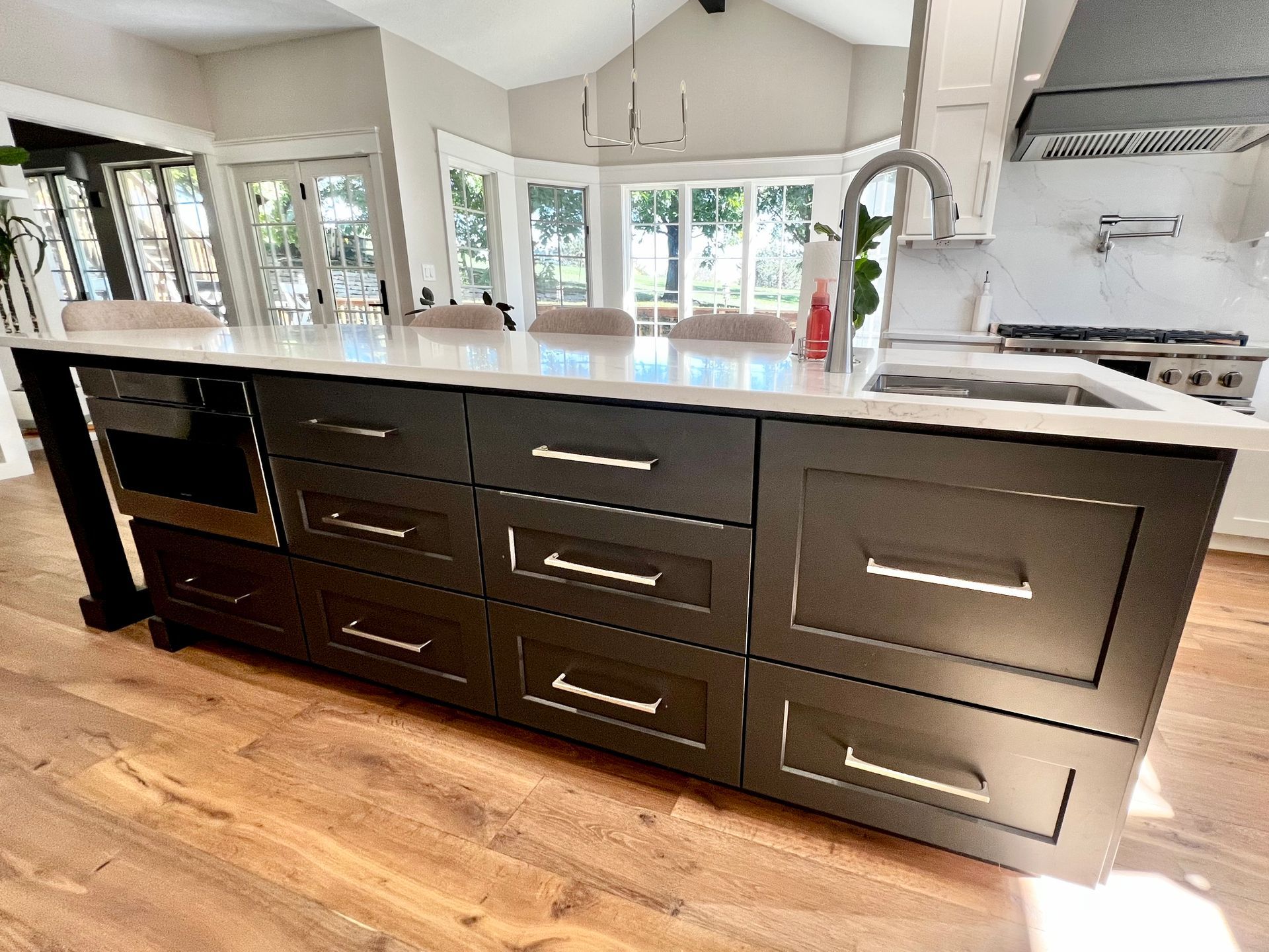 Dark kitchen island with a white countertop and silver hardware in a bright, modern open-plan home.