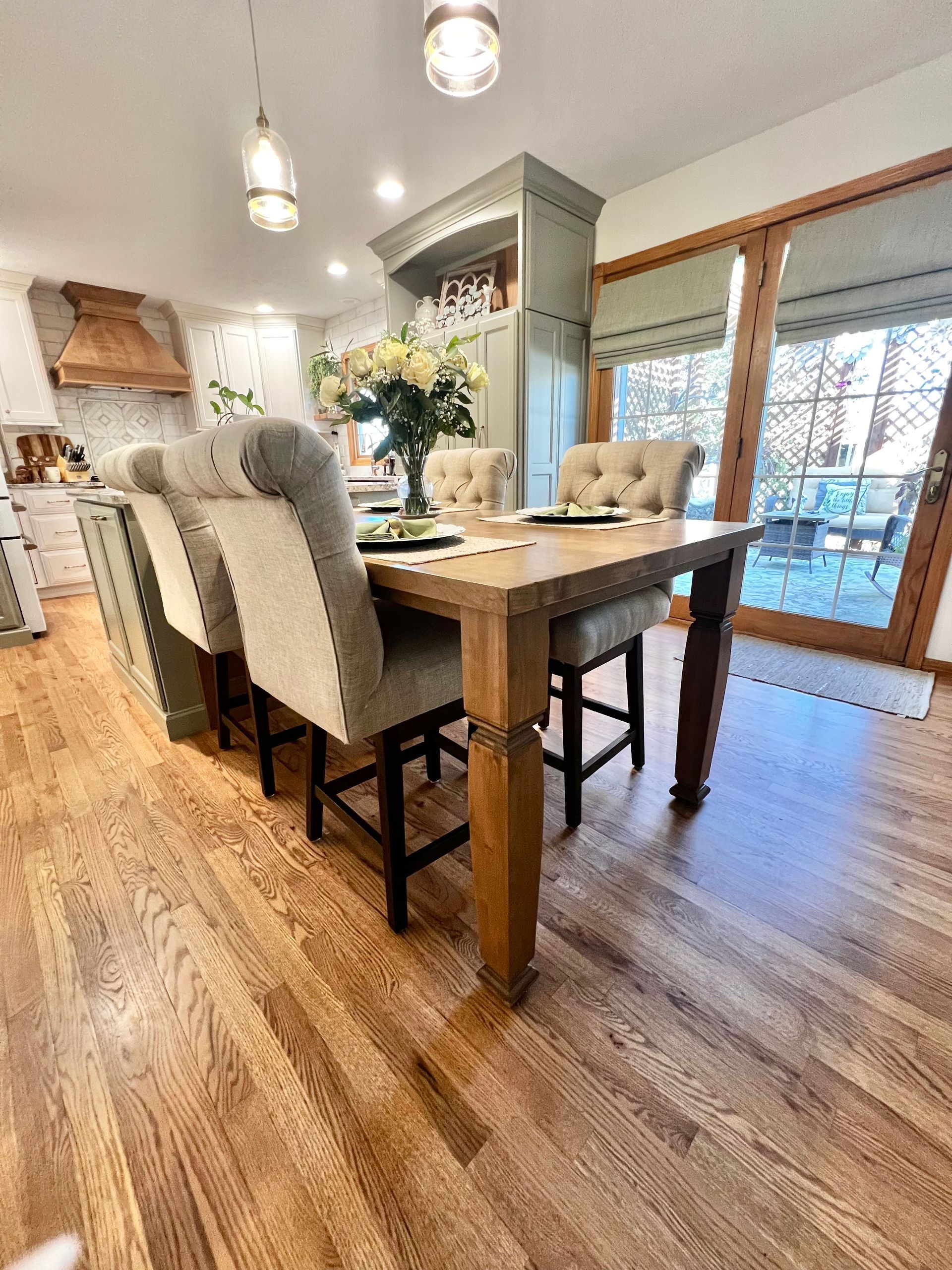 A dining table set with upholstered chairs in a brightly lit kitchen with hardwood floors and sliding glass doors.