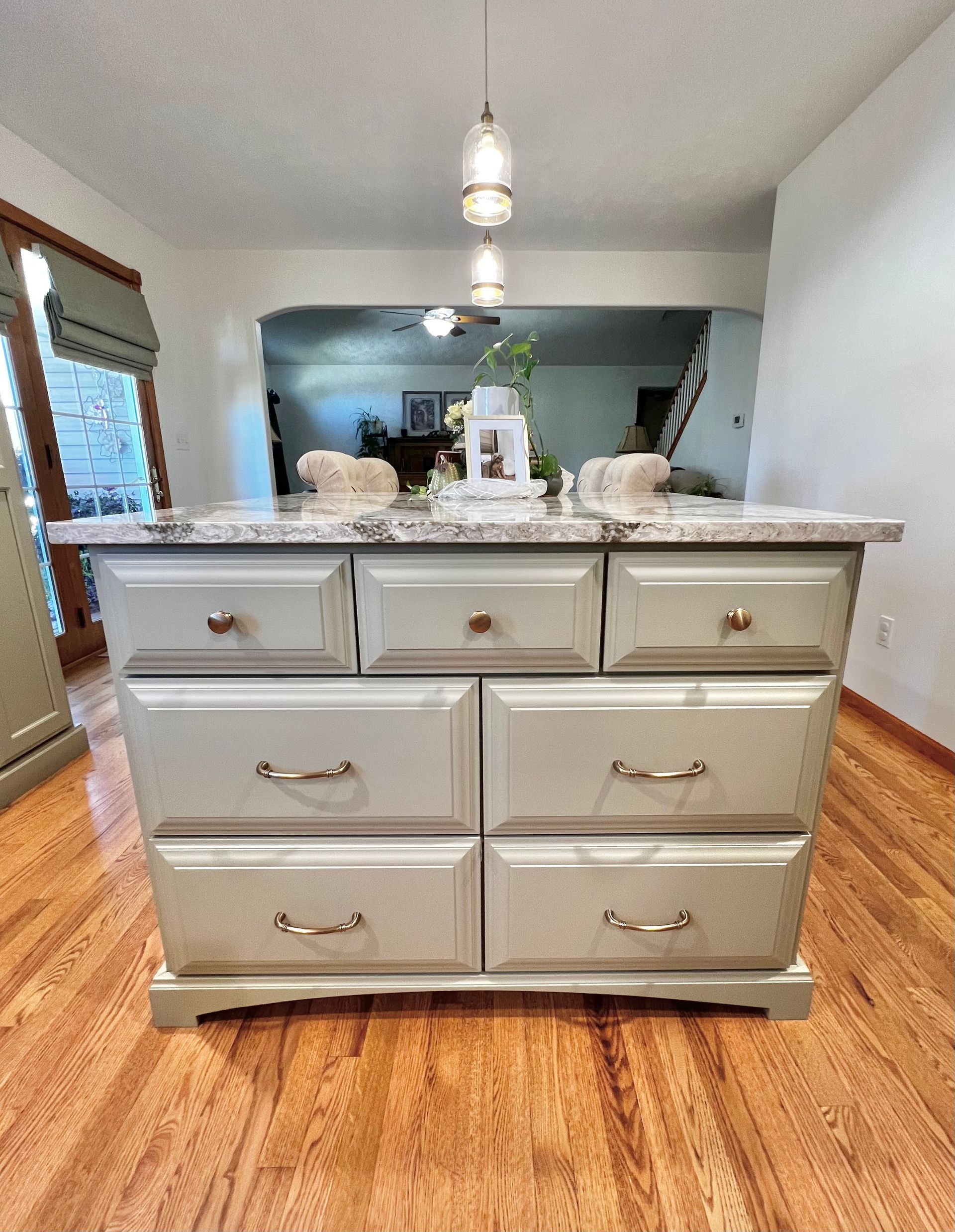 A grey kitchen island with a granite countertop, featuring three small top drawers and four larger drawers below.