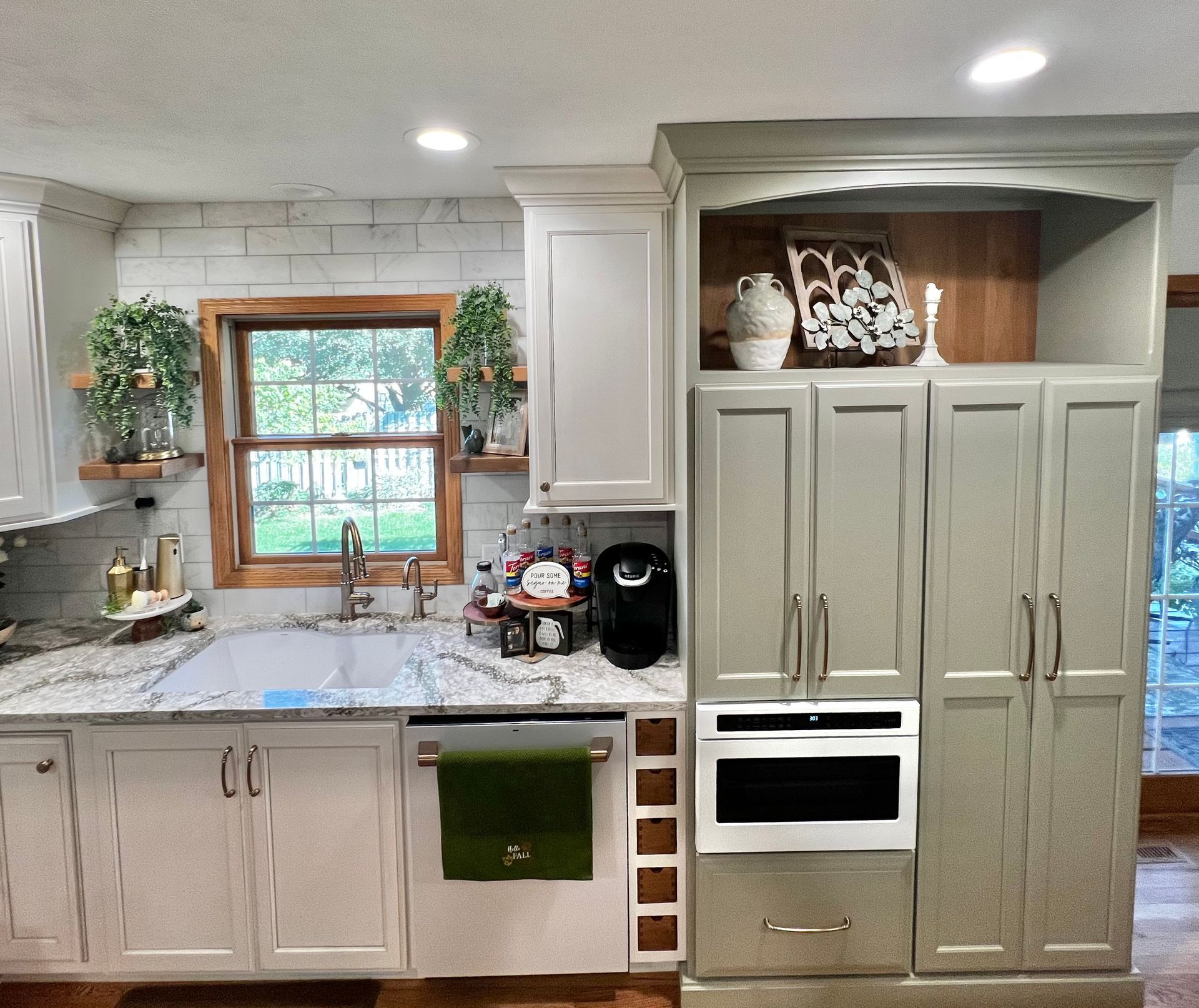 A kitchen with white cabinets, granite countertops, a farmhouse sink, and a built-in microwave/pantry unit in light gray.