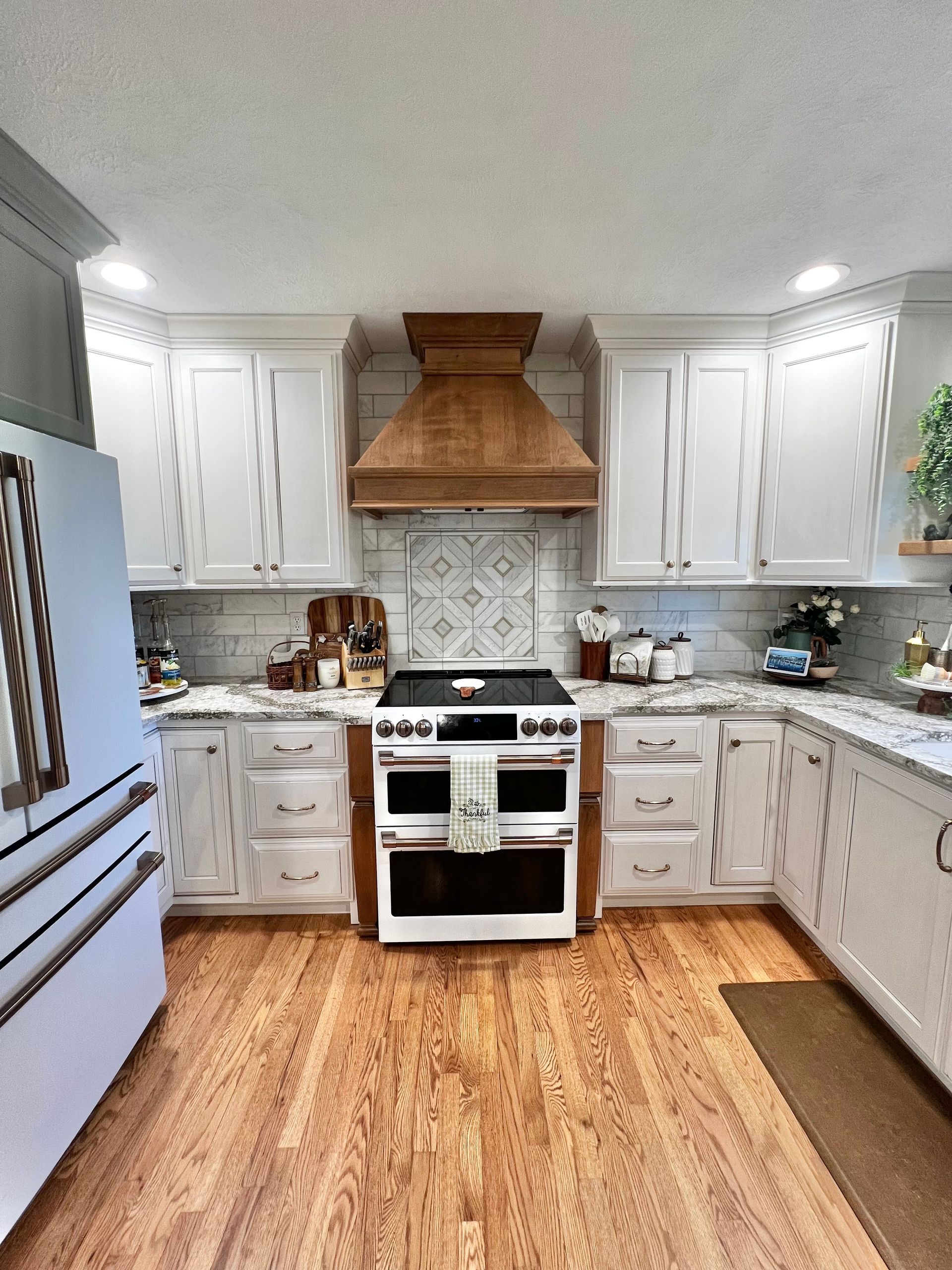 A kitchen with white cabinets, a wood range hood, a stainless steel double oven, and wood-patterned flooring.