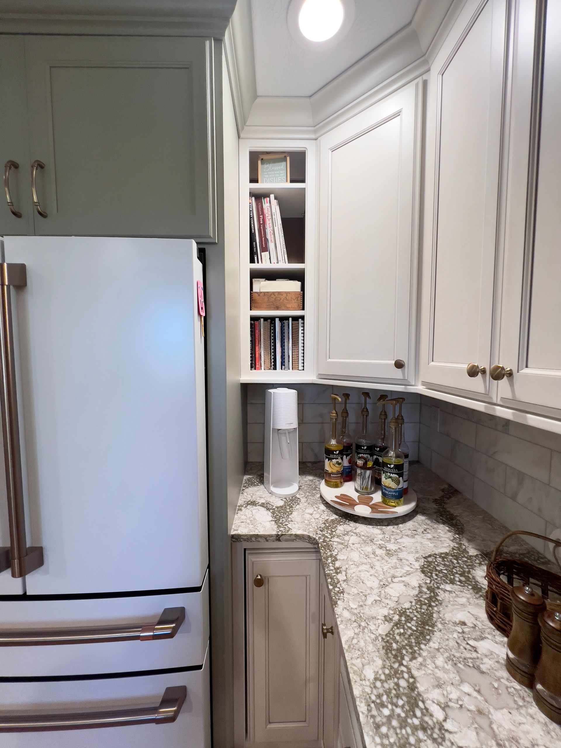 A kitchen corner showing a white refrigerator, open shelving, and a granite countertop with a small drink station.