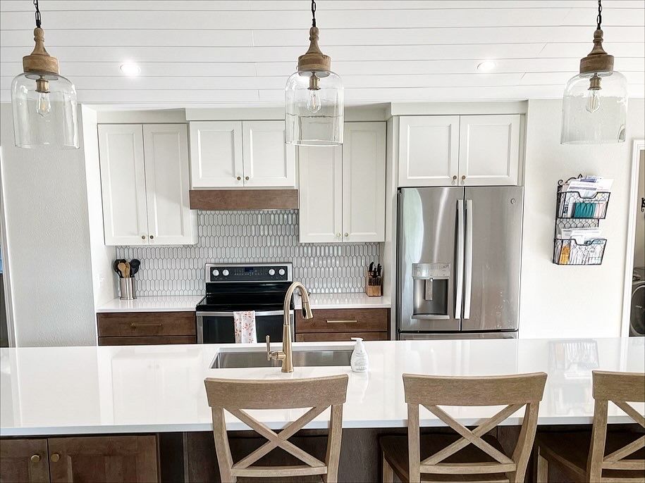 Modern kitchen with a white island, wooden bar stools, white cabinetry, dark lower cabinets, and stainless steel appliances.