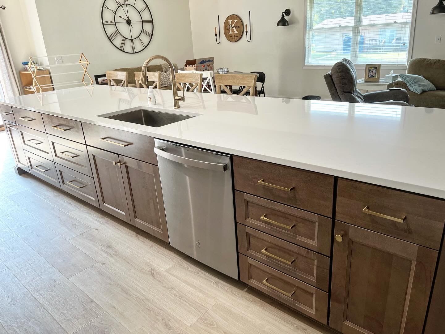A long kitchen island with a white countertop, wooden cabinets, a stainless steel sink, and a dishwasher.