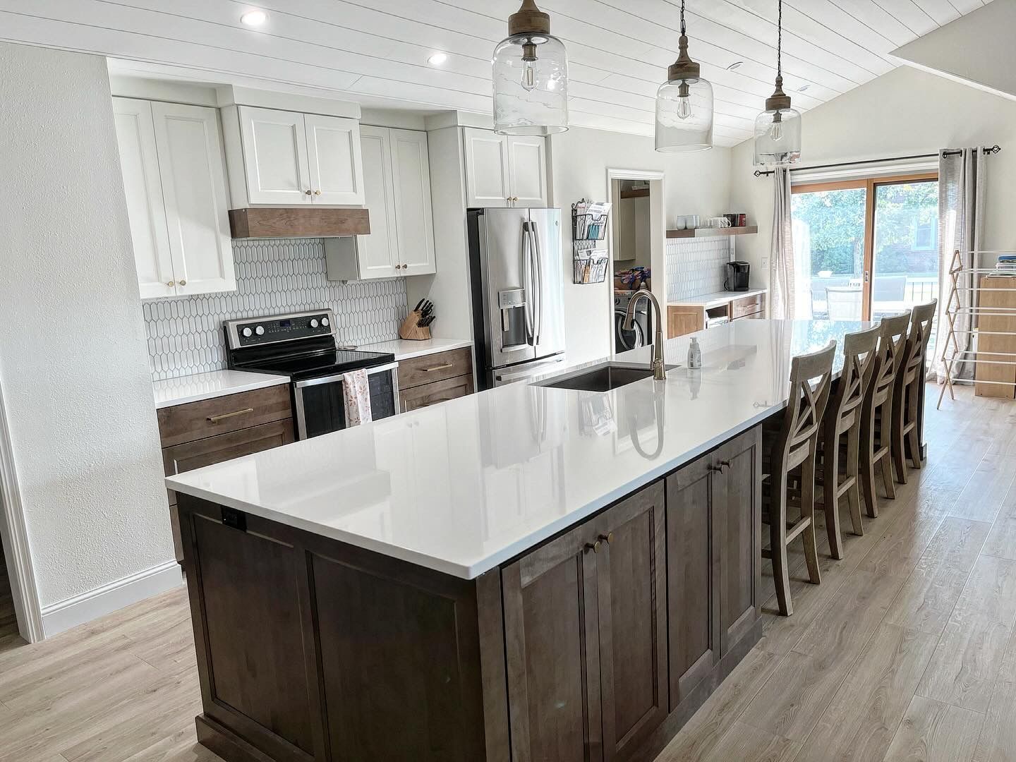 A kitchen featuring a large dark wood island with a white countertop, three pendant lights, and bar stools.