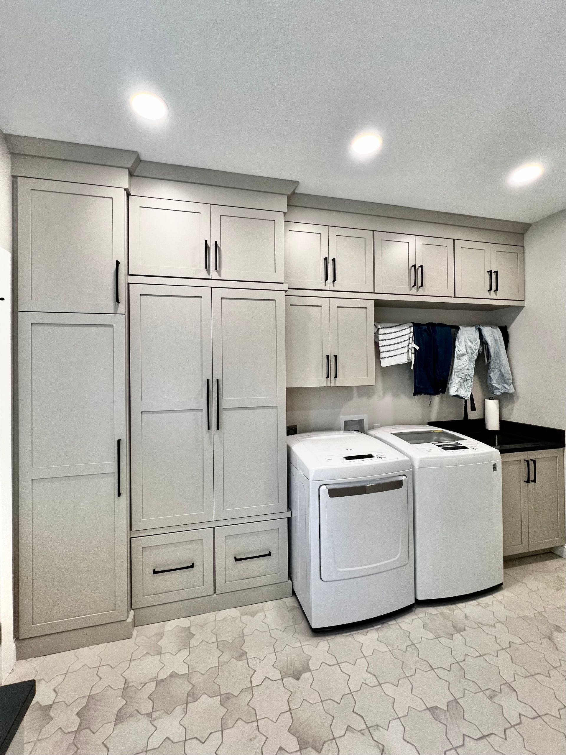 A laundry room featuring light gray cabinetry, a matching washer and dryer, and patterned tile flooring.