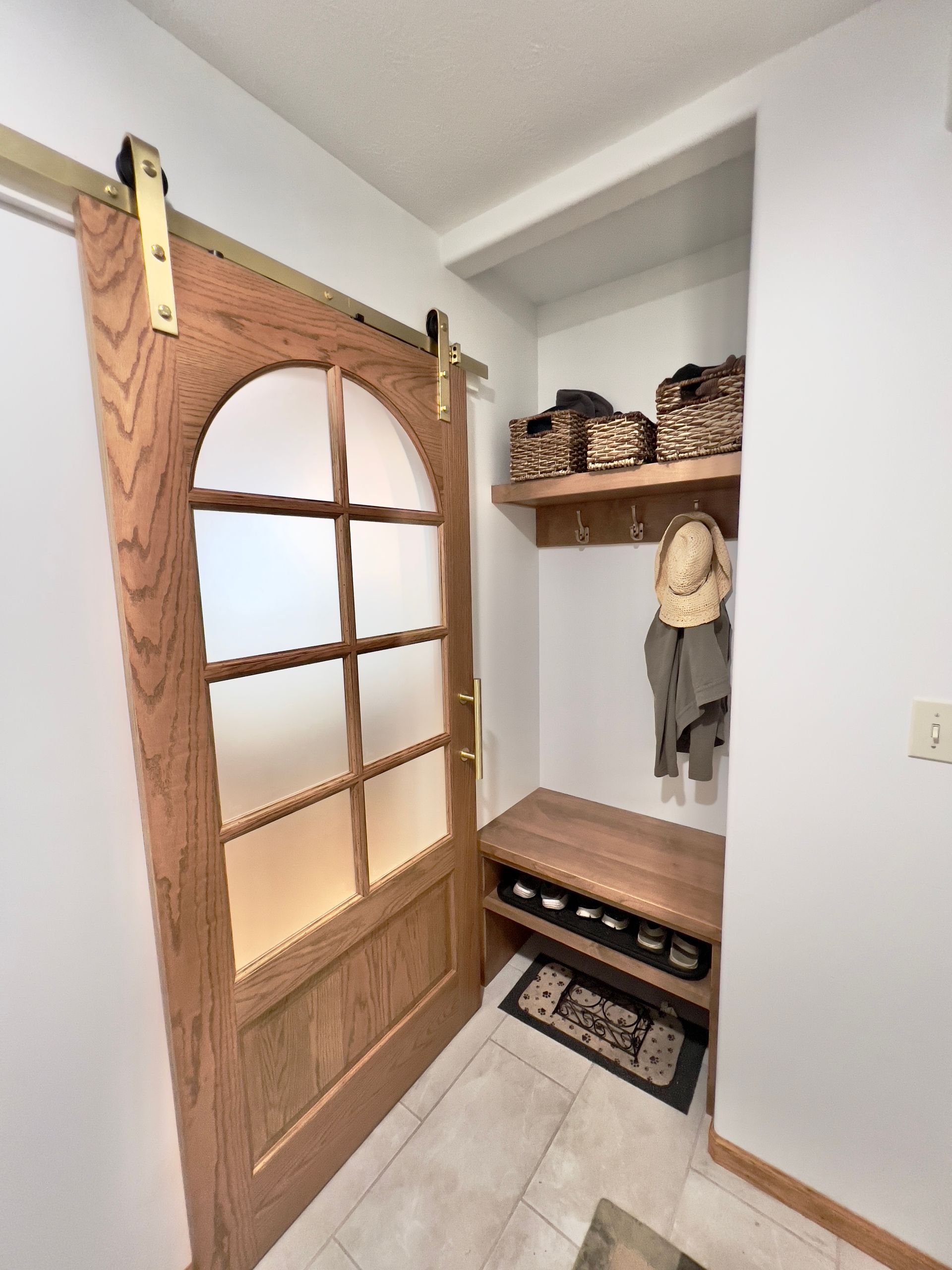A wooden sliding barn door with glass panels next to a small mudroom nook featuring a bench, coat hooks, and storage bins.