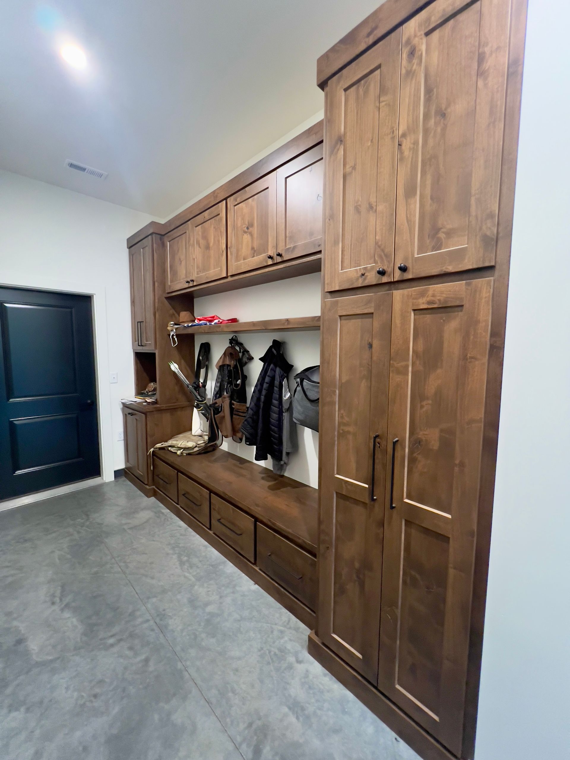 Custom wood mudroom storage featuring a bench, coat hooks, and floor-to-ceiling cabinets against a white wall.