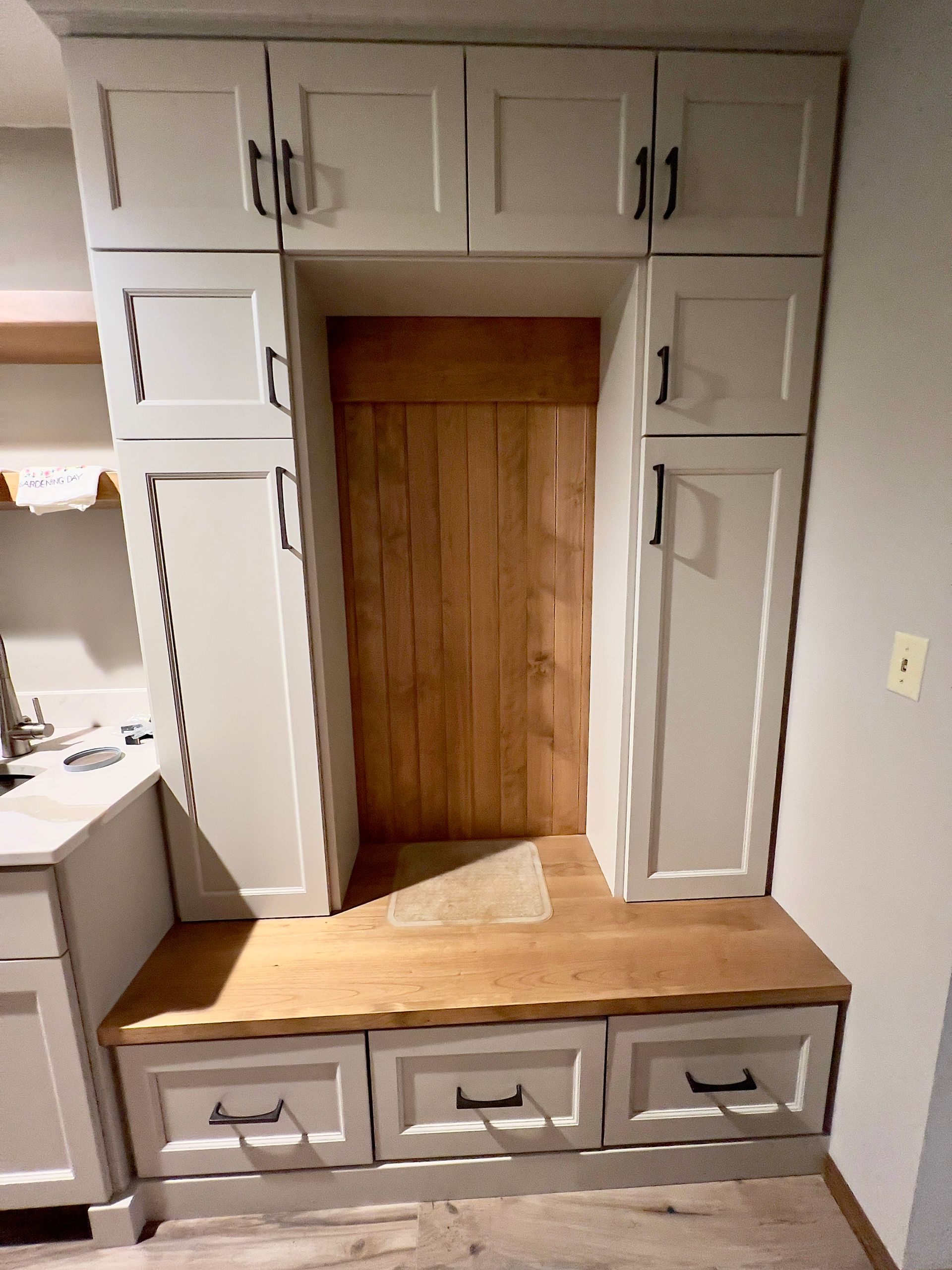 A white built-in mudroom bench with natural wood backing and seating, featuring upper and lower storage cabinets.