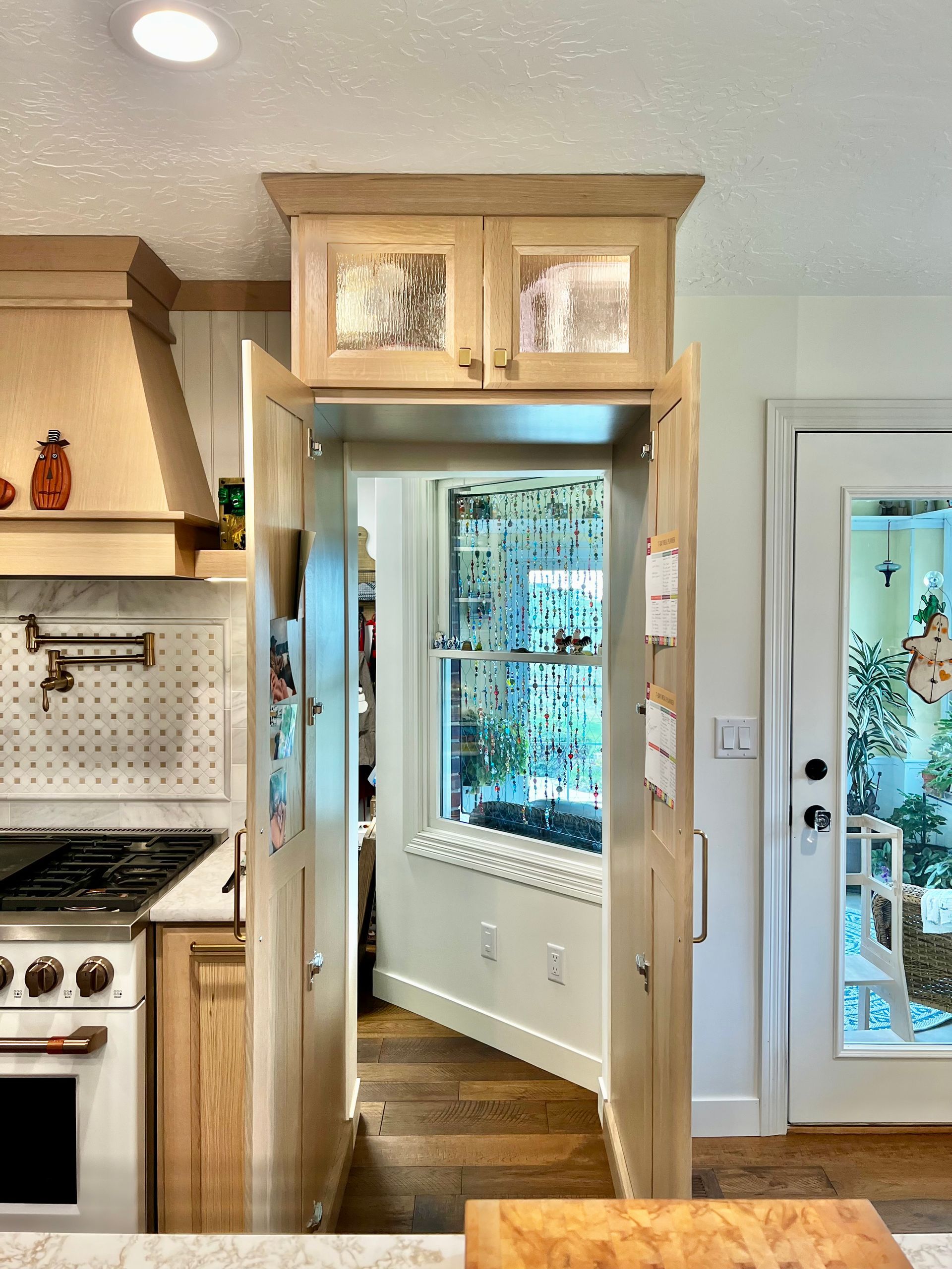 An open, light-wood cabinetry frame serving as a doorway to a bright sunroom with a window and plants.