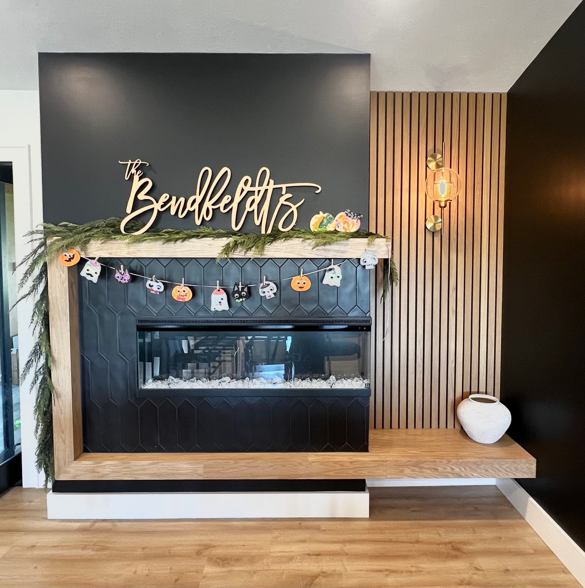 A fireplace with black tiles, a light wood mantle, a 