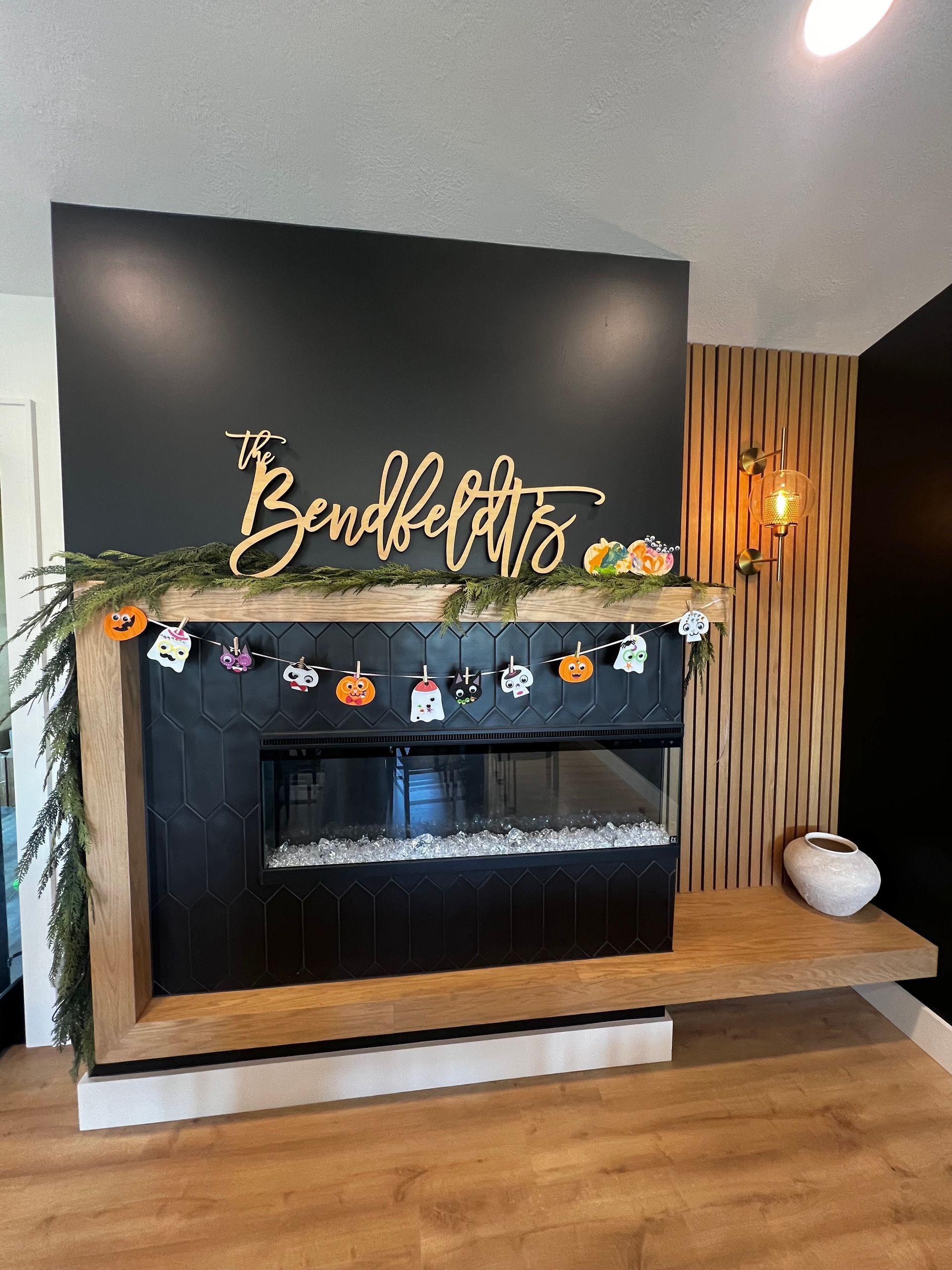 Modern fireplace with a black tile surround, wood mantle, name sign, and hanging Halloween decorations.