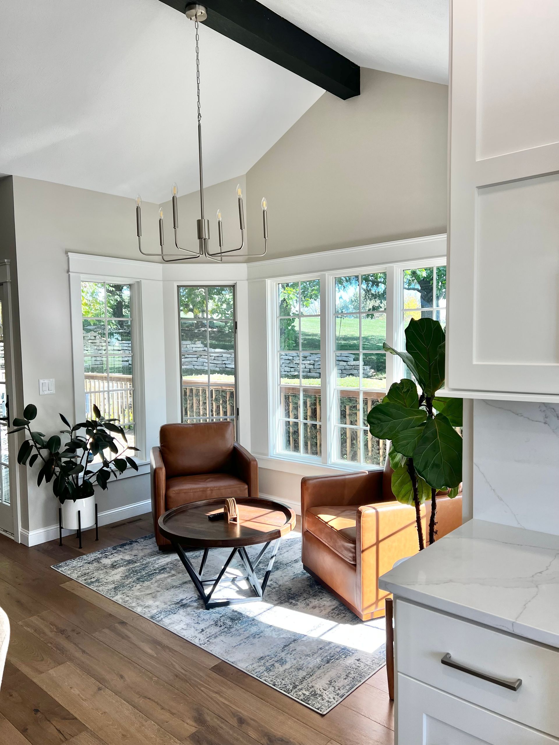 A sunlit corner featuring two brown leather armchairs, a round coffee table, and an area rug near large windows.
