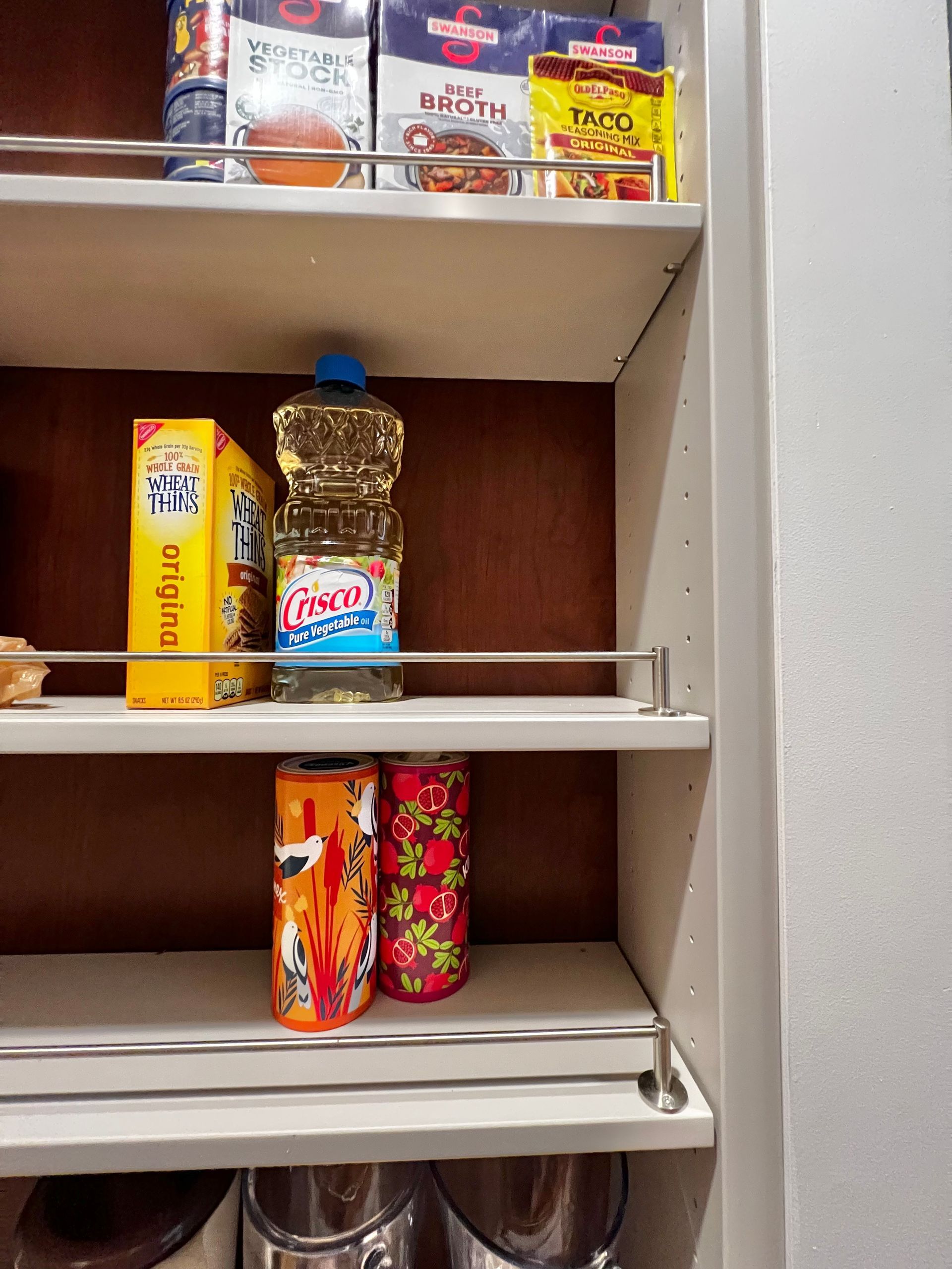 Pantry shelves with various food items including cartons of stock, a bottle of vegetable oil, and floral-patterned cans.