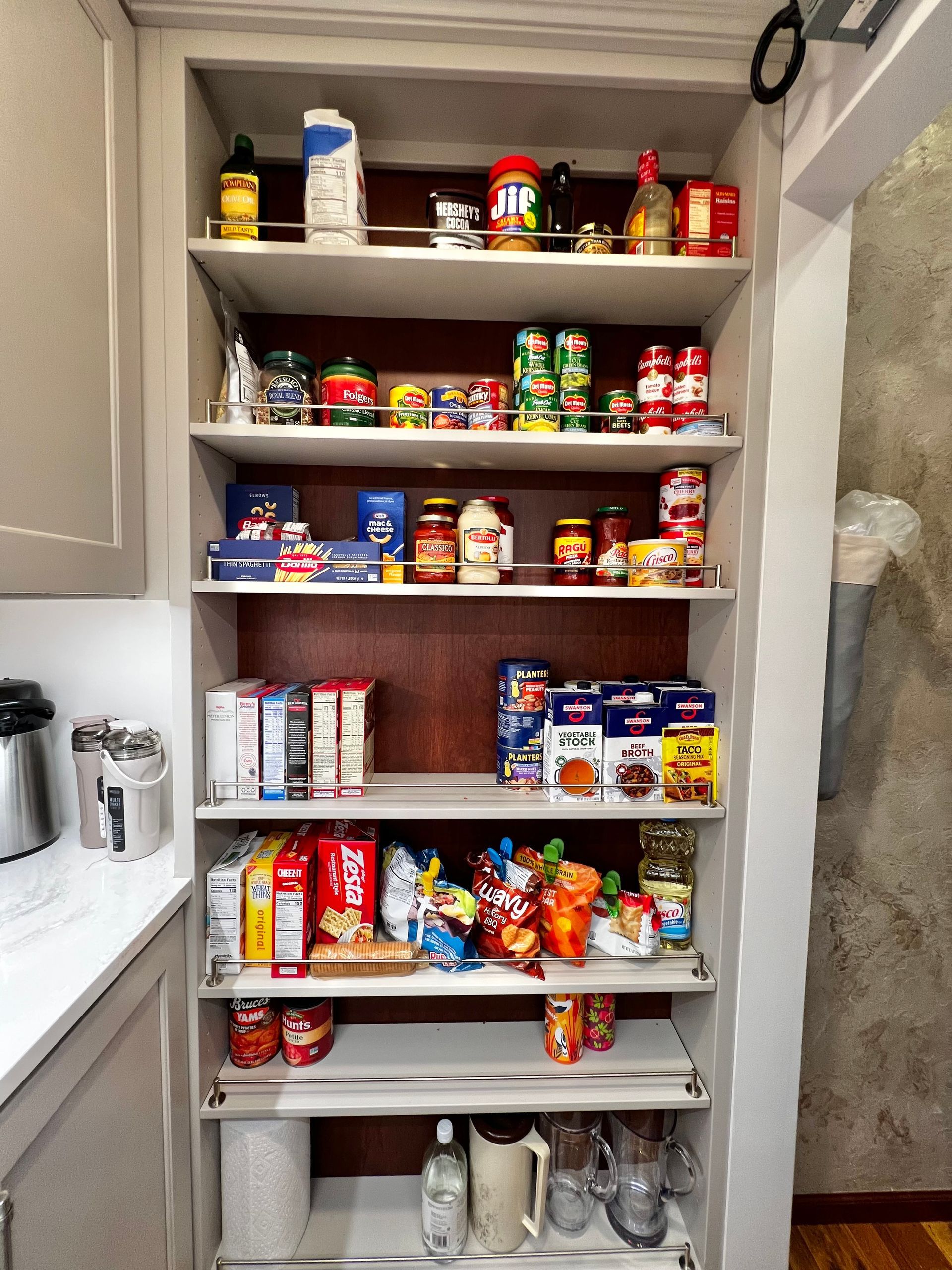 A tall, organized kitchen pantry shelf filled with various food items, containers, and household goods.