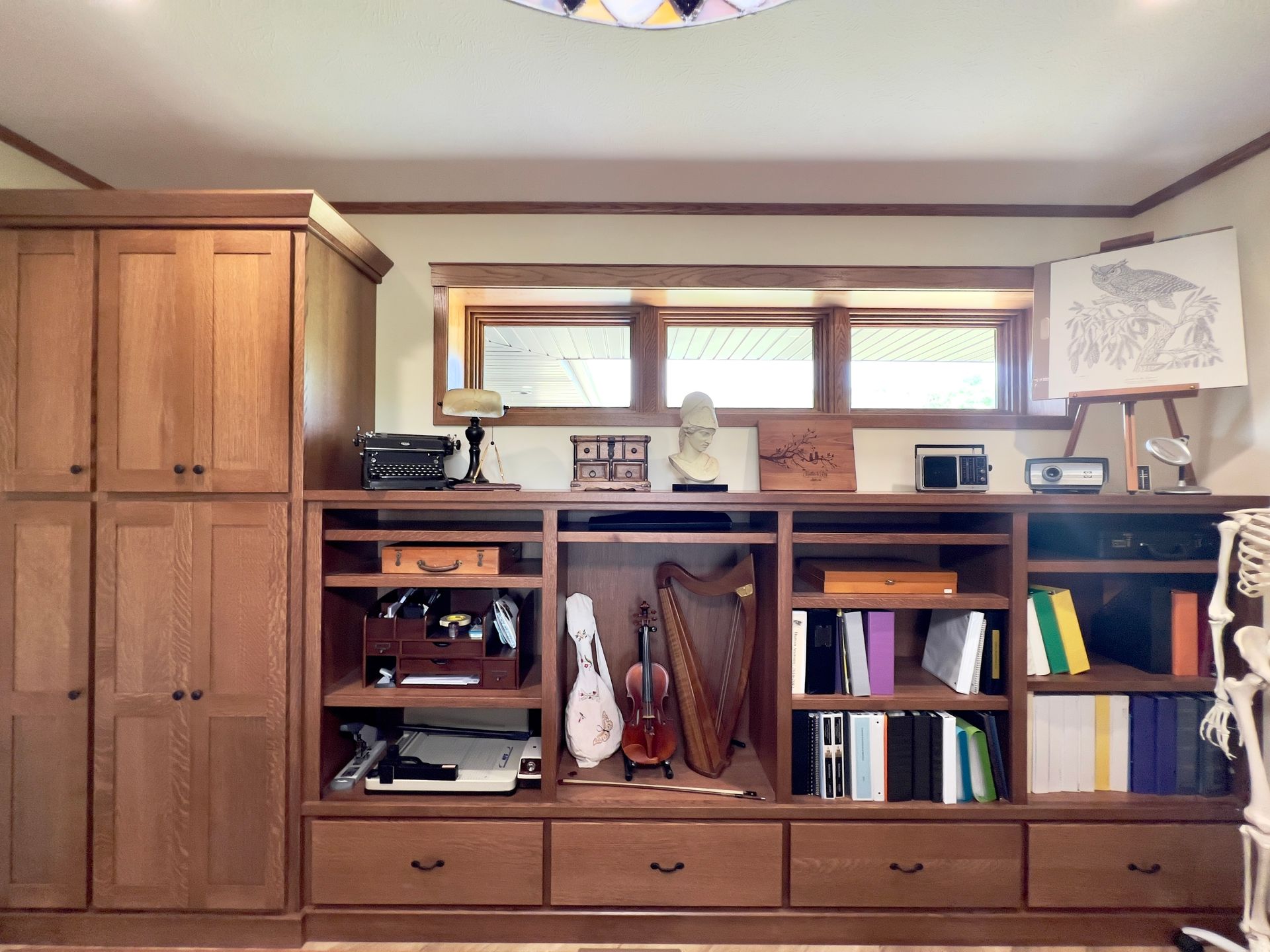 A large wooden wall unit with cabinets, open shelves holding books and musical instruments, and drawers below.