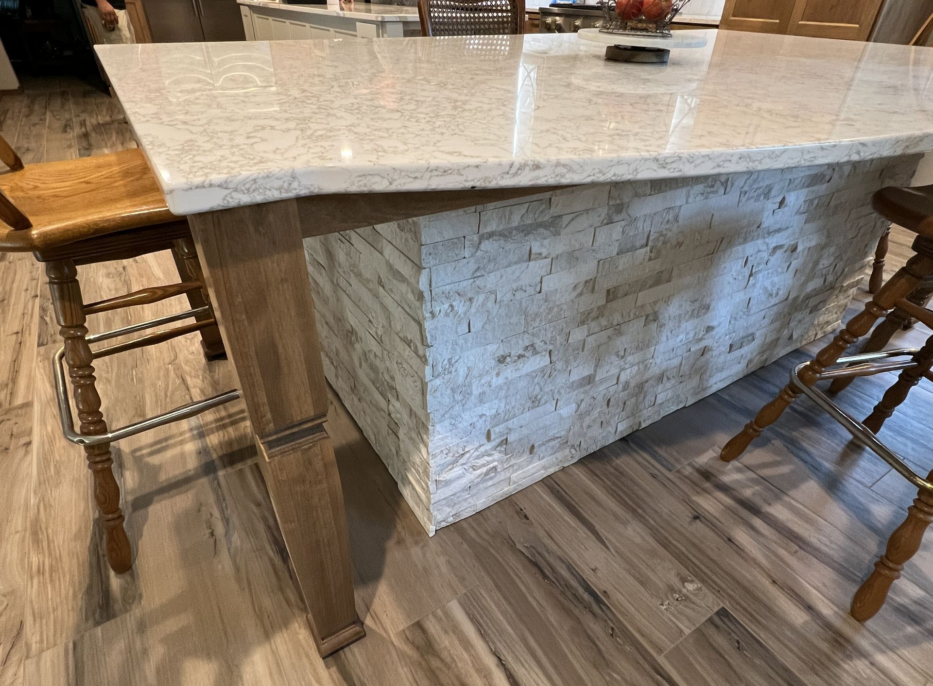 A kitchen island with a speckled white countertop, a light-colored stone base, and two wooden bar stools on a wood floor.