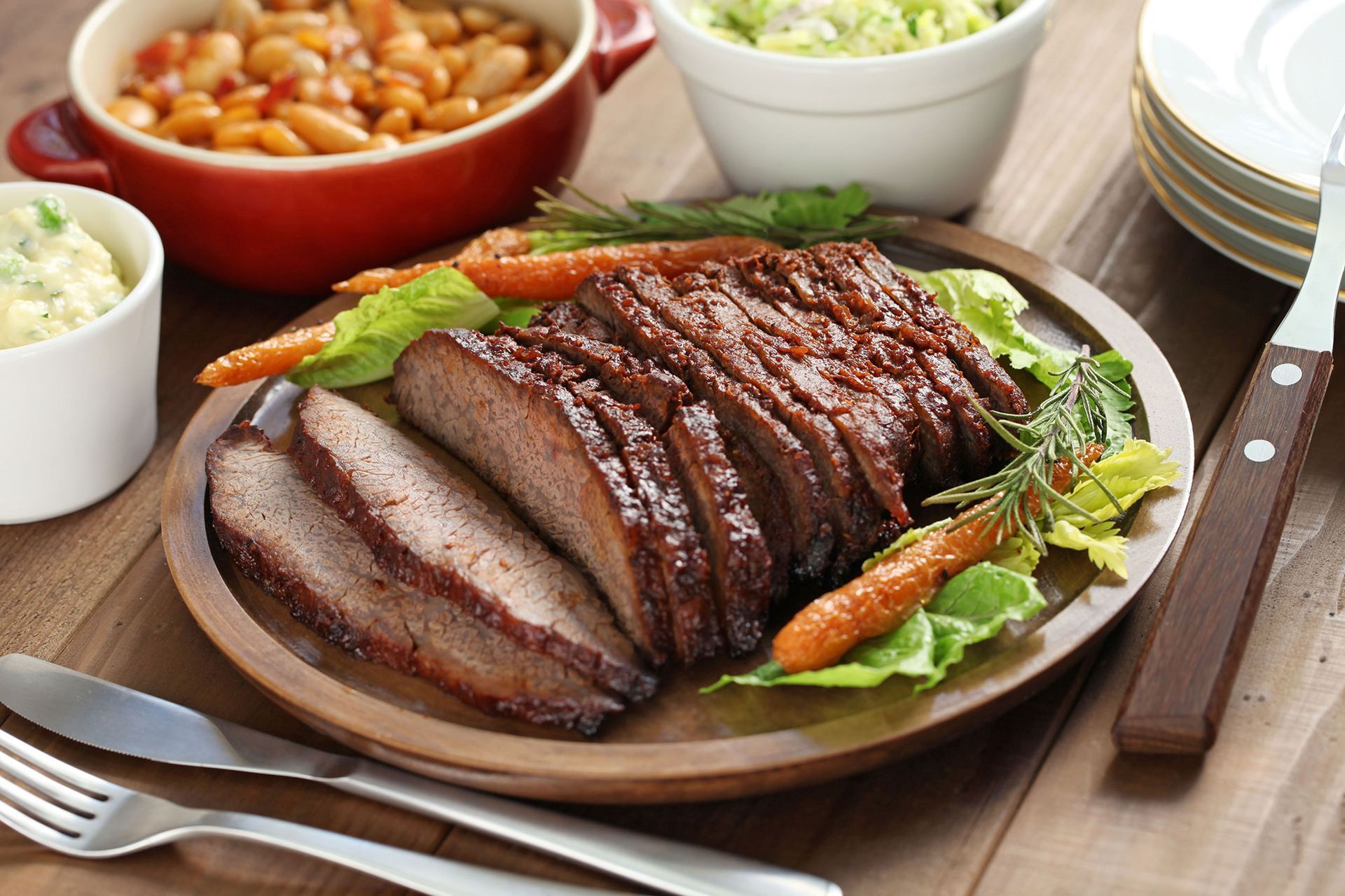 A plate of sliced brisket with carrots and lettuce on a wooden table.