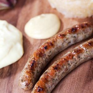 Two sausages are sitting on a wooden table next to a bowl of mayonnaise.