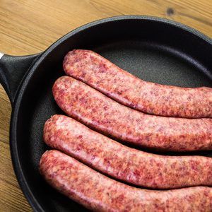 Four sausages are sitting in a frying pan on a wooden table.