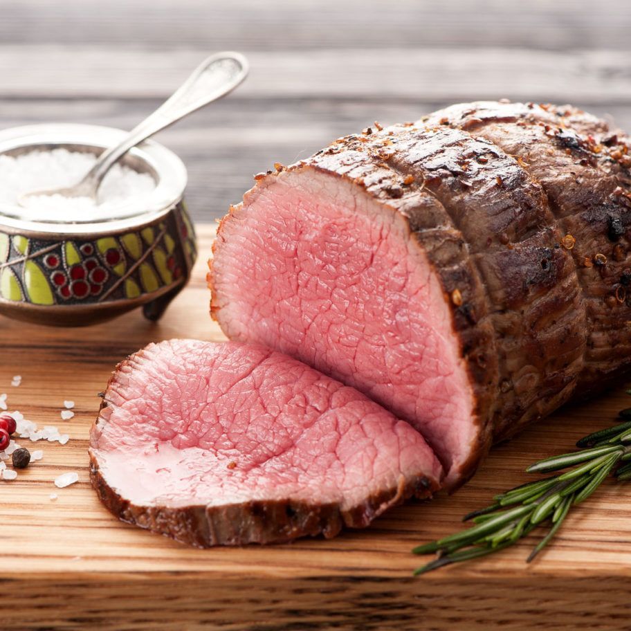 A large piece of roast beef is sitting on a wooden cutting board.