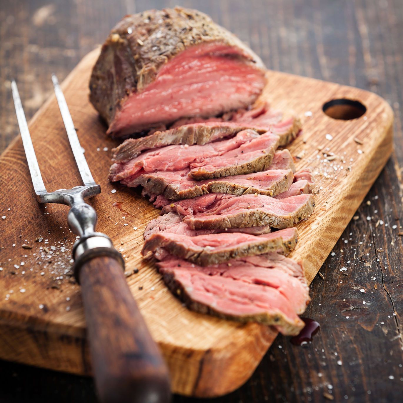 Sliced roast beef on a wooden cutting board with a fork