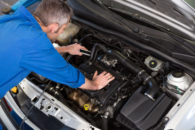 Mechanic in blue shirt working under the hood of a car in a garage