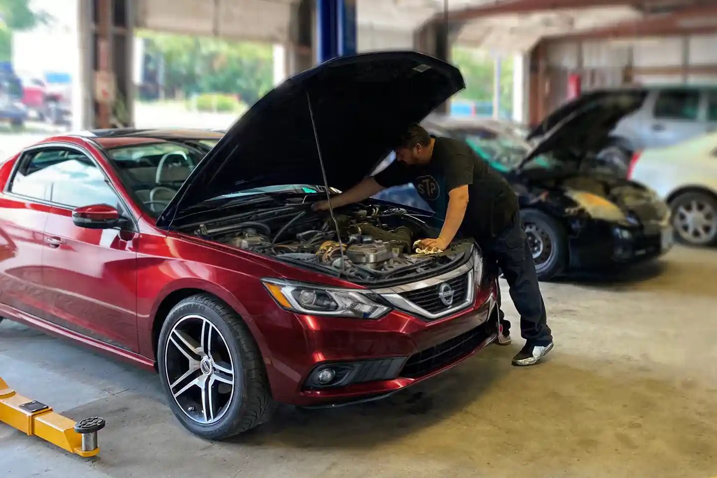 Red sedan with hood open as a mechanic inspects the engine in a garage.