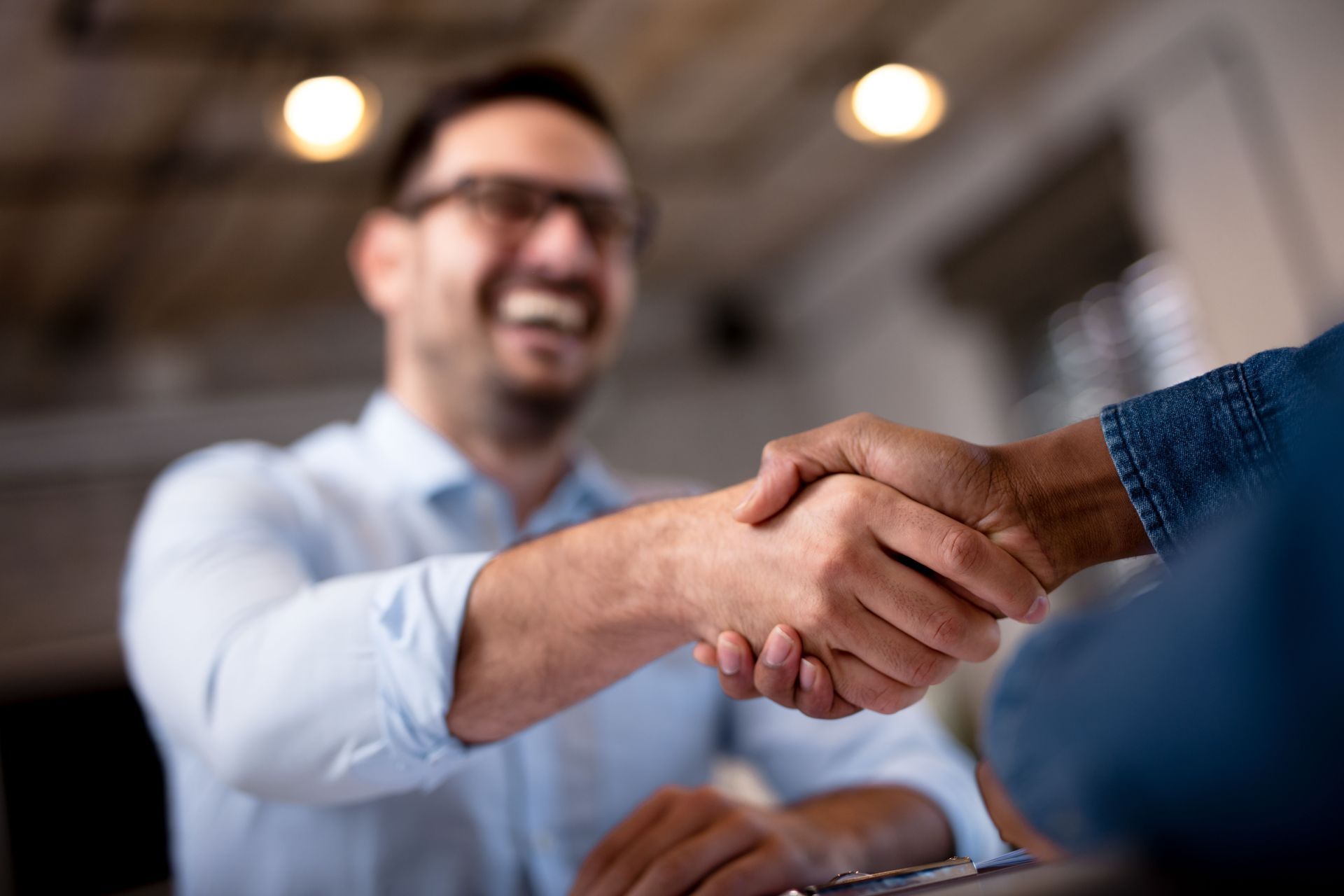 Two people shaking hands in a bright office, with one smiling in the background