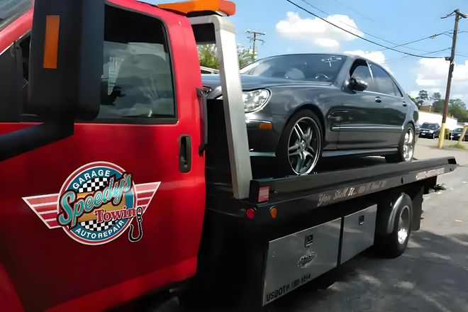 Red tow truck carrying a dark gray car on a flatbed by the roadside