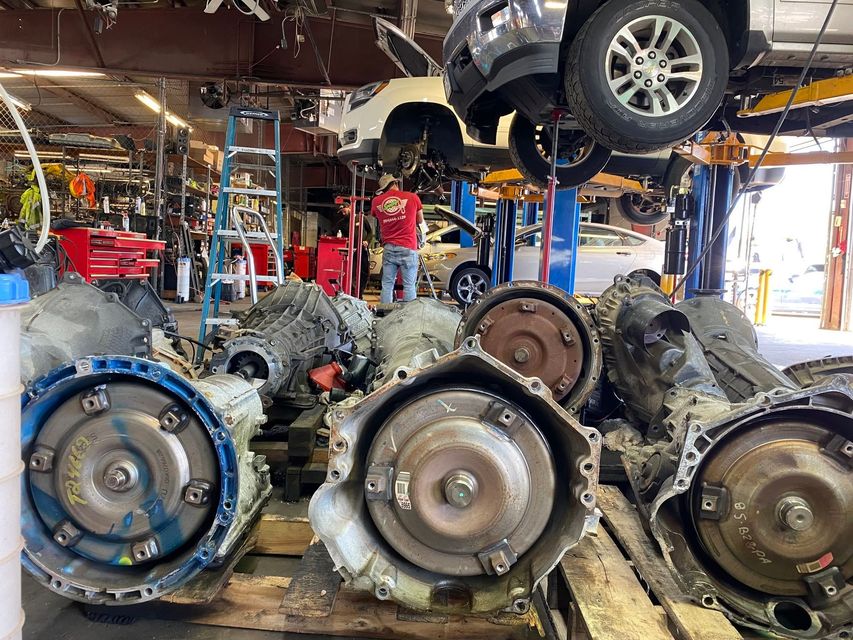 Auto repair shop with several car transmissions and a car lifted overhead on a hoist